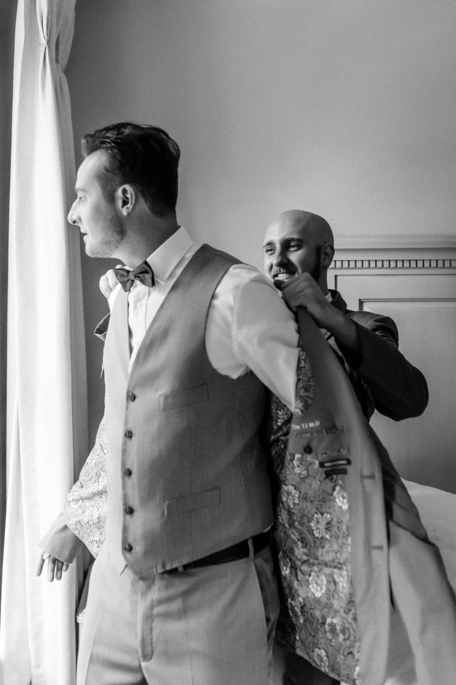 Black and white photo of groomsman helping adjust groom's attire.