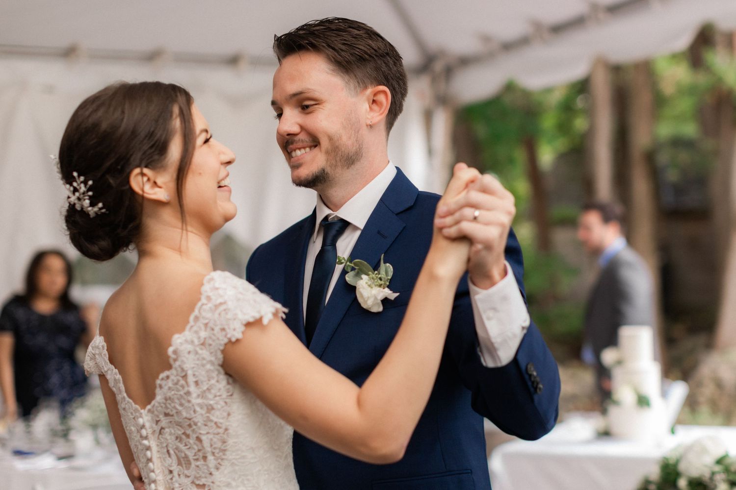 A couple shares their first dance under a white tent reception at their wedding celebration.