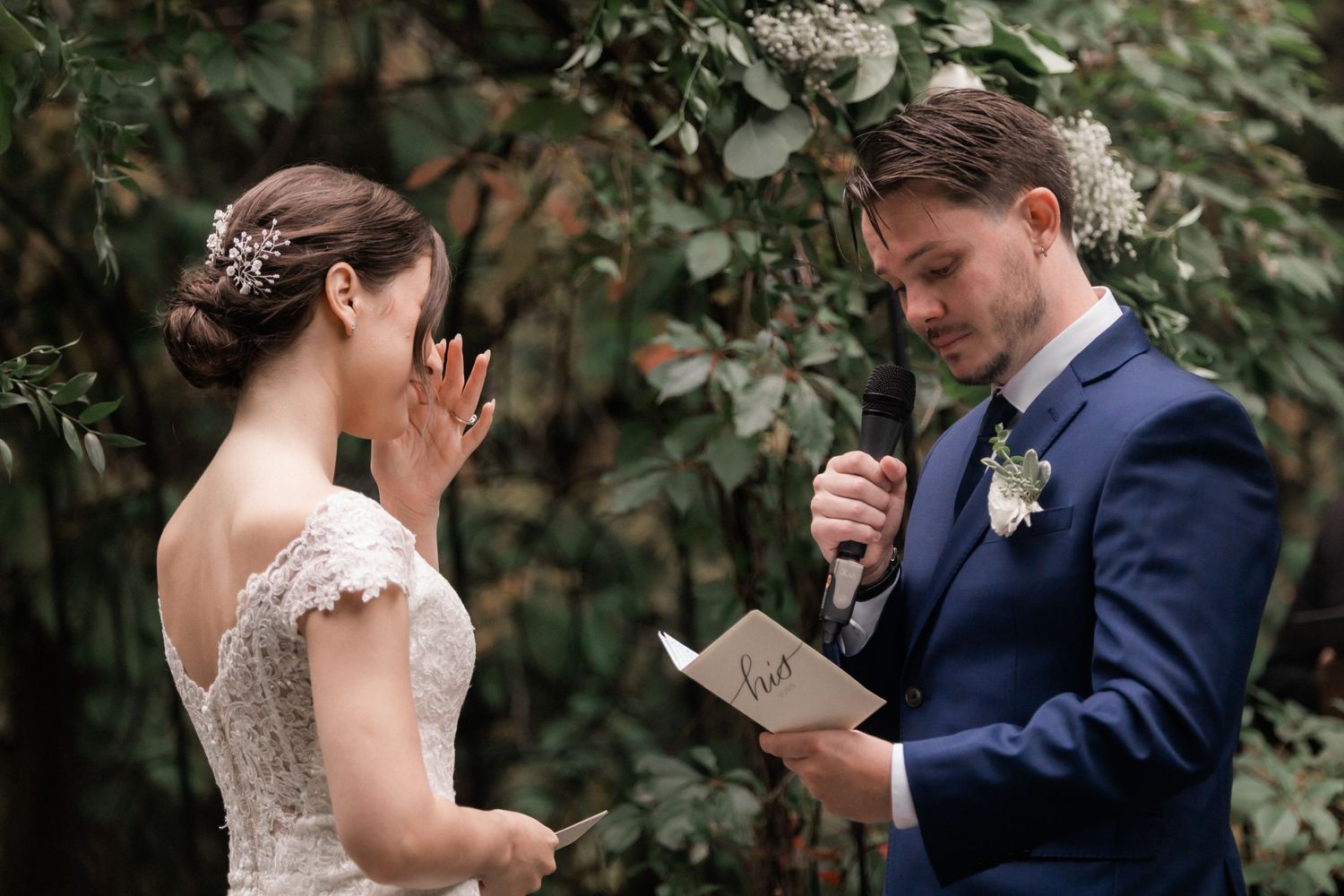 An emotional wedding ceremony moment captured under a floral arch in a garden setting.