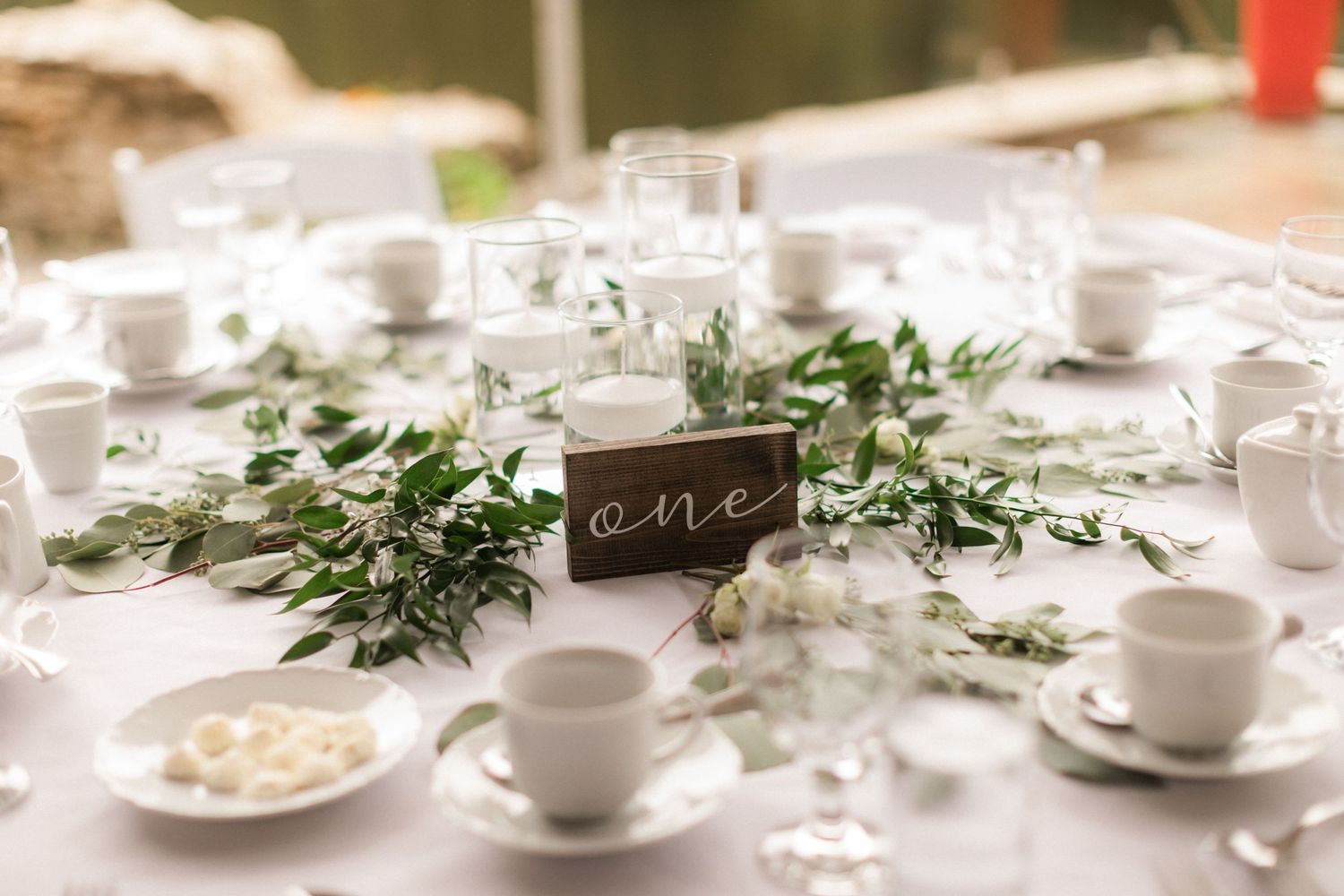 Wedding table setting with greenery garland, white teacups, and rustic table number.