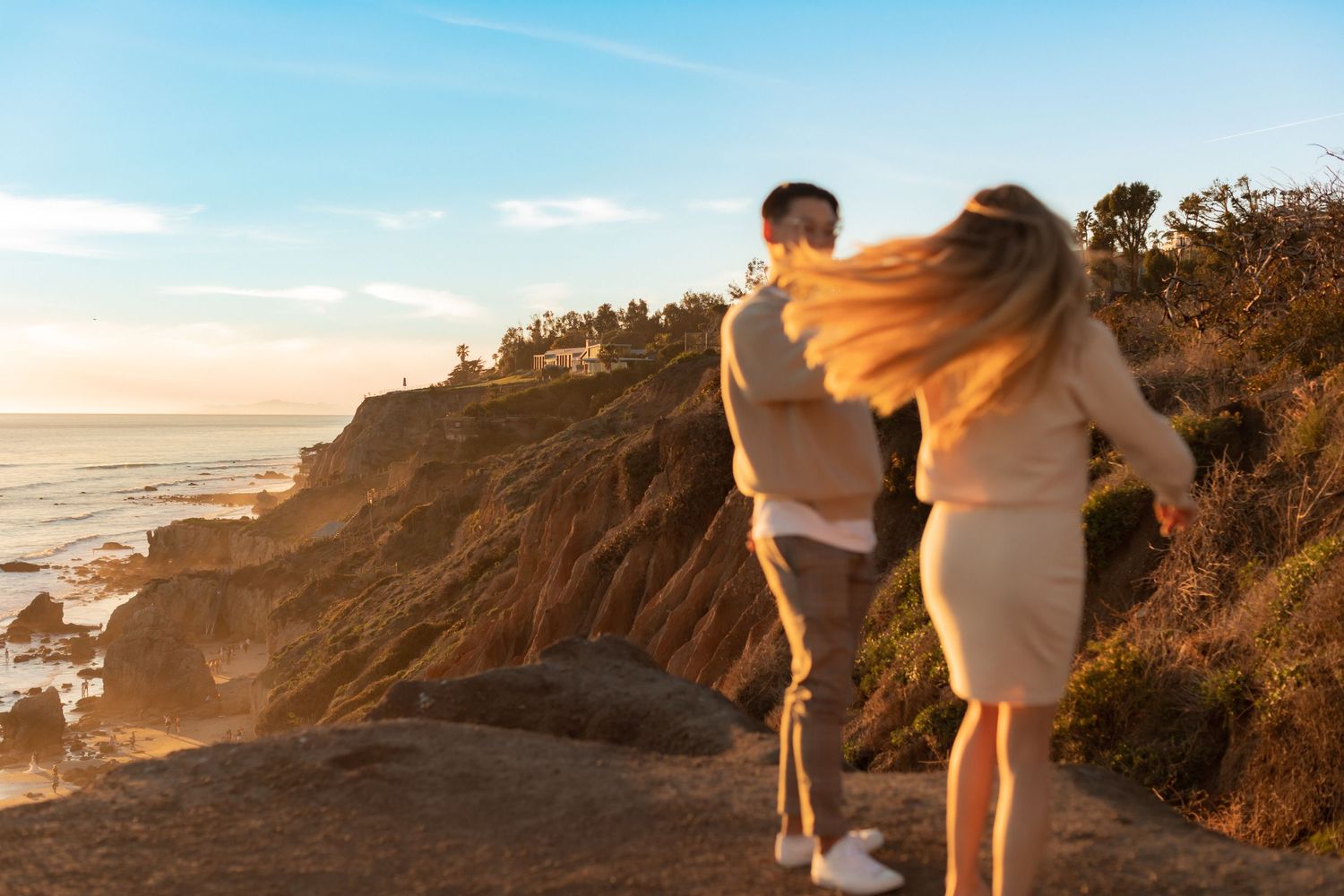 Couple exploring rocky coastal path during golden hour sunset.