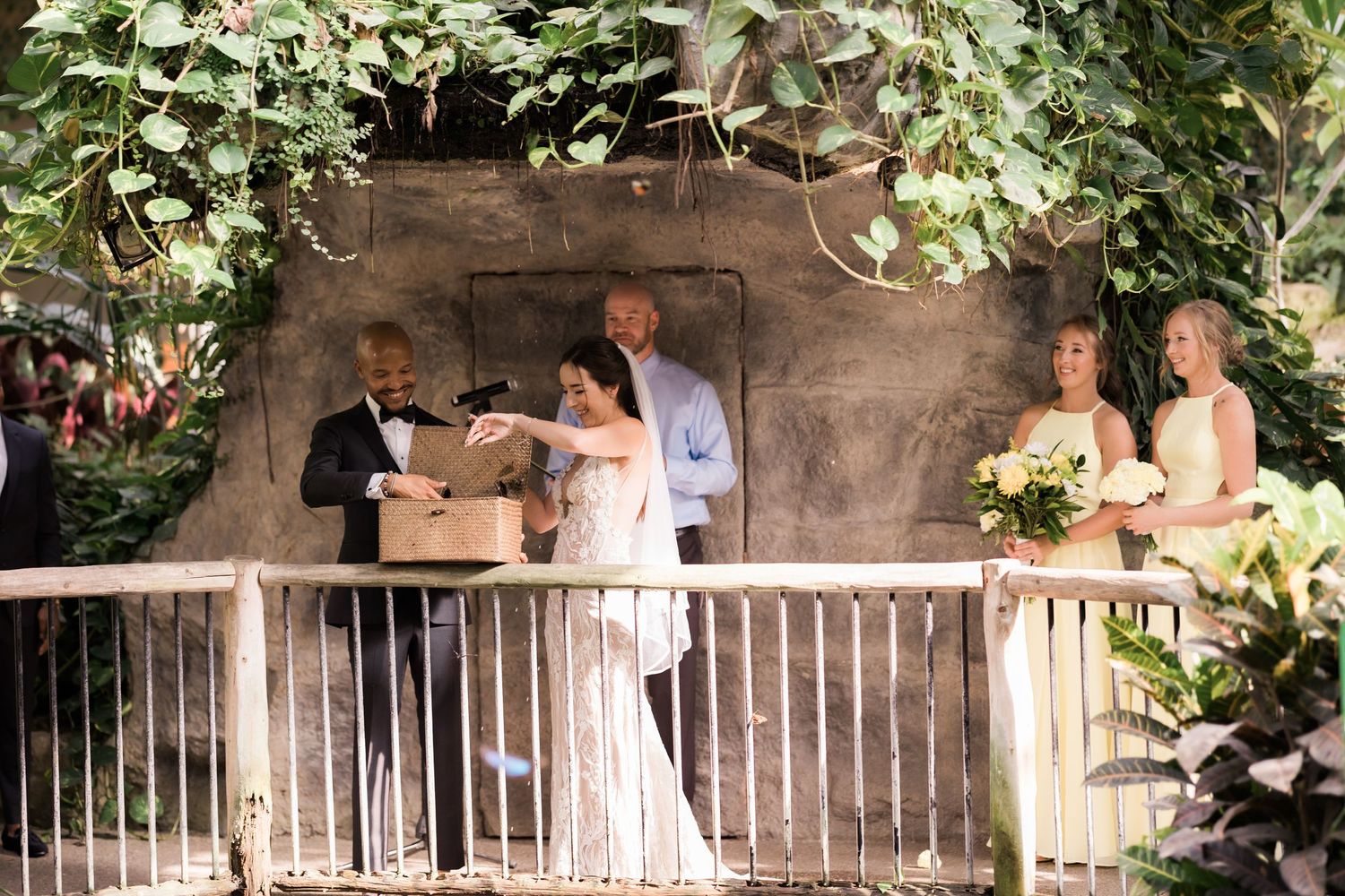 Wedding ceremony in progress on decorated stone balcony with attendants.
