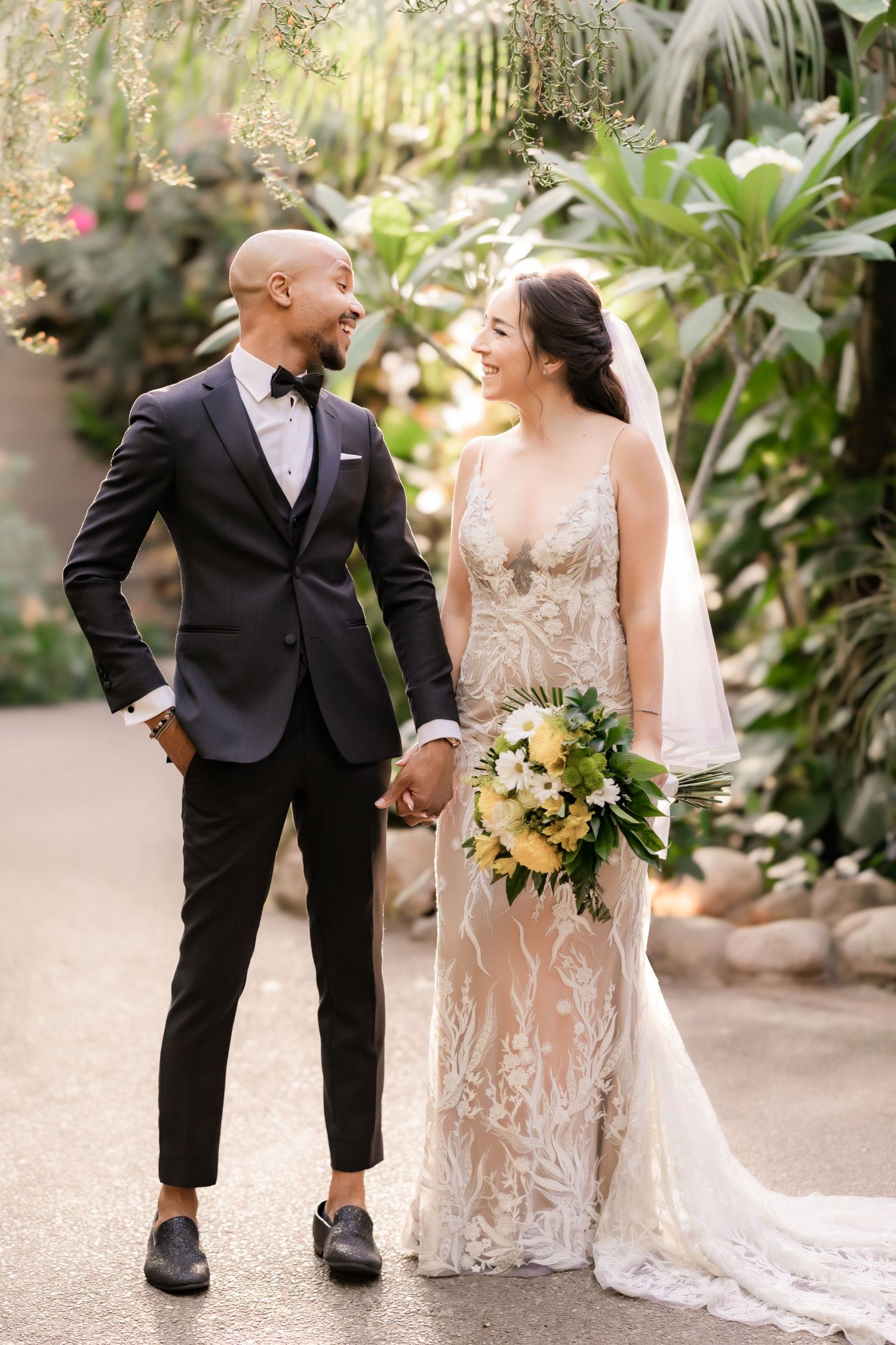 A newlywed couple shares a laugh while posing in a botanical garden setting.