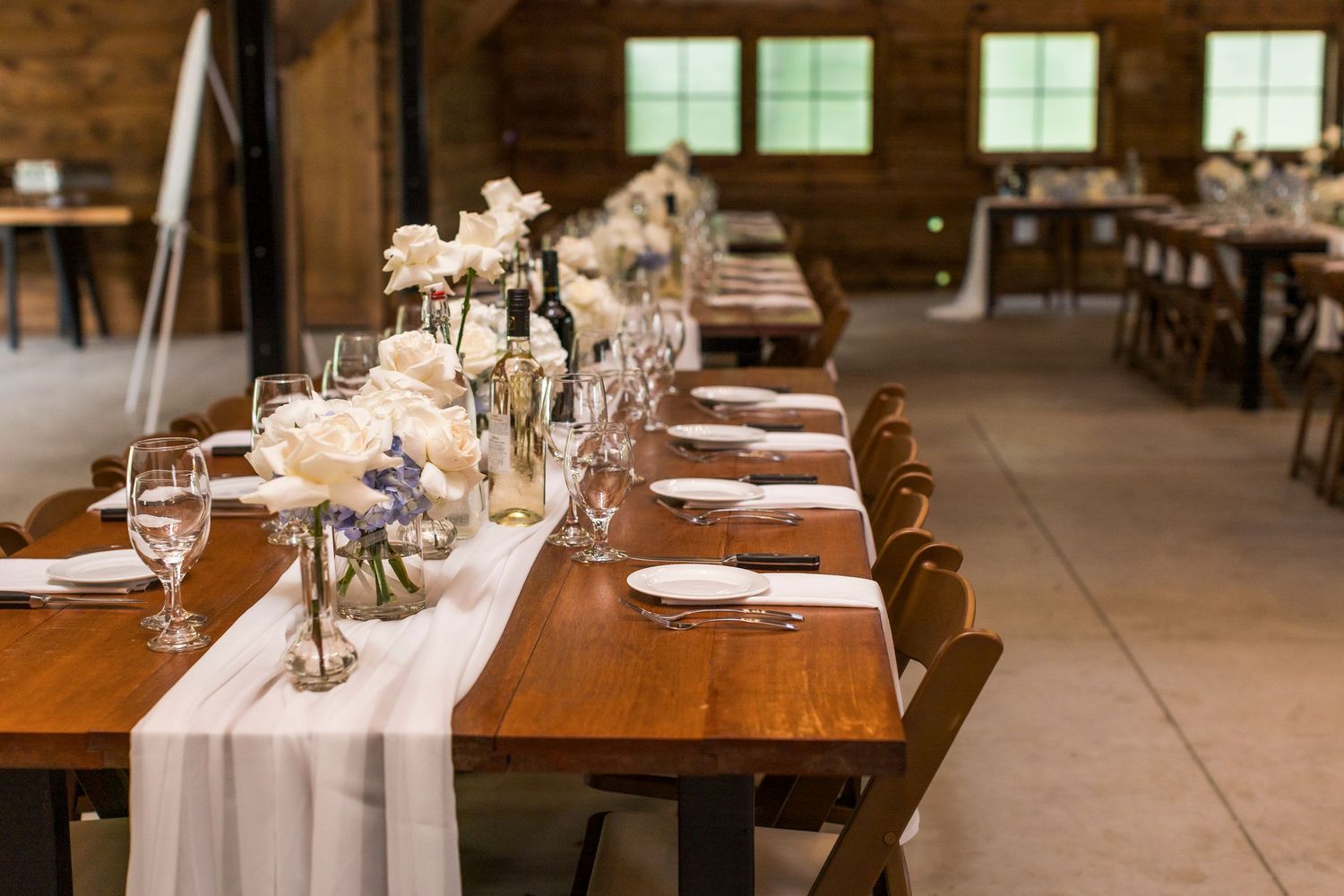 Elegant rustic wedding reception setup with wooden tables decorated with white runners and floral centerpieces.