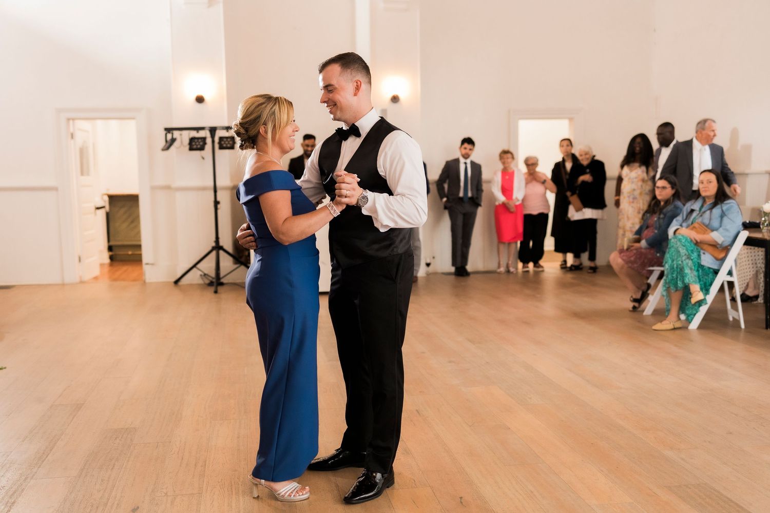 A couple dancing together in an elegant ballroom with light wood floors and white walls.