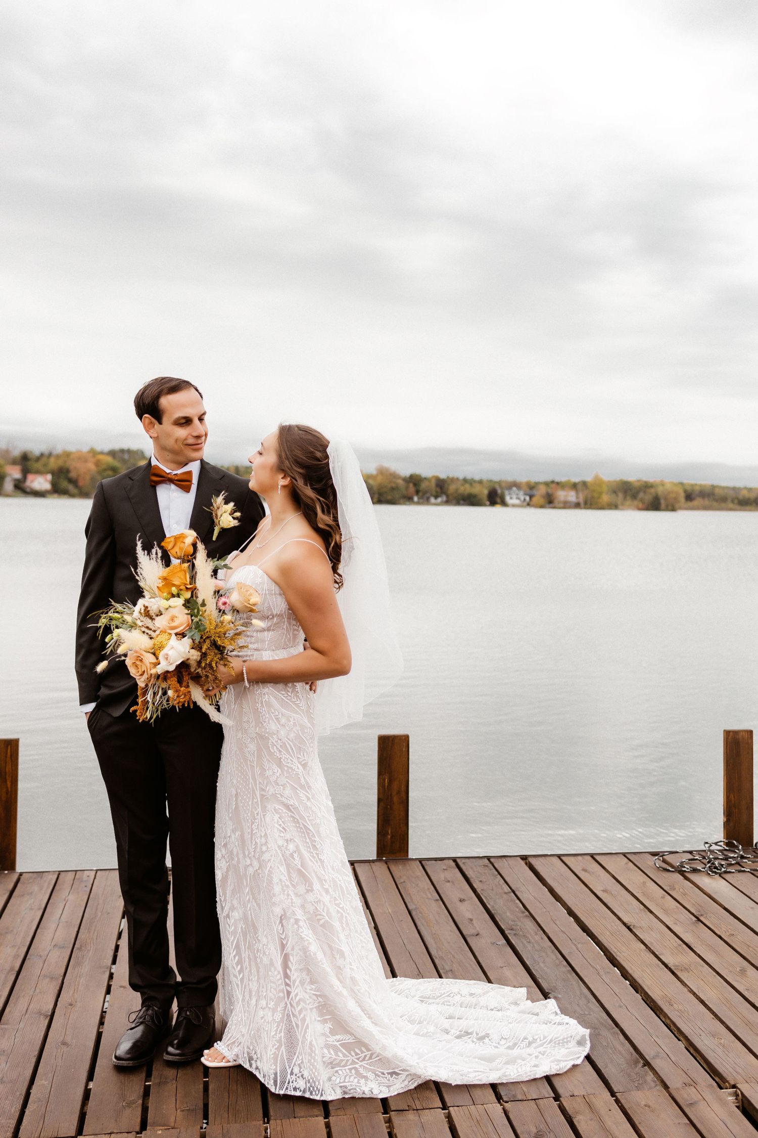 Newlyweds share an intimate moment on a lakeside dock during autumn.