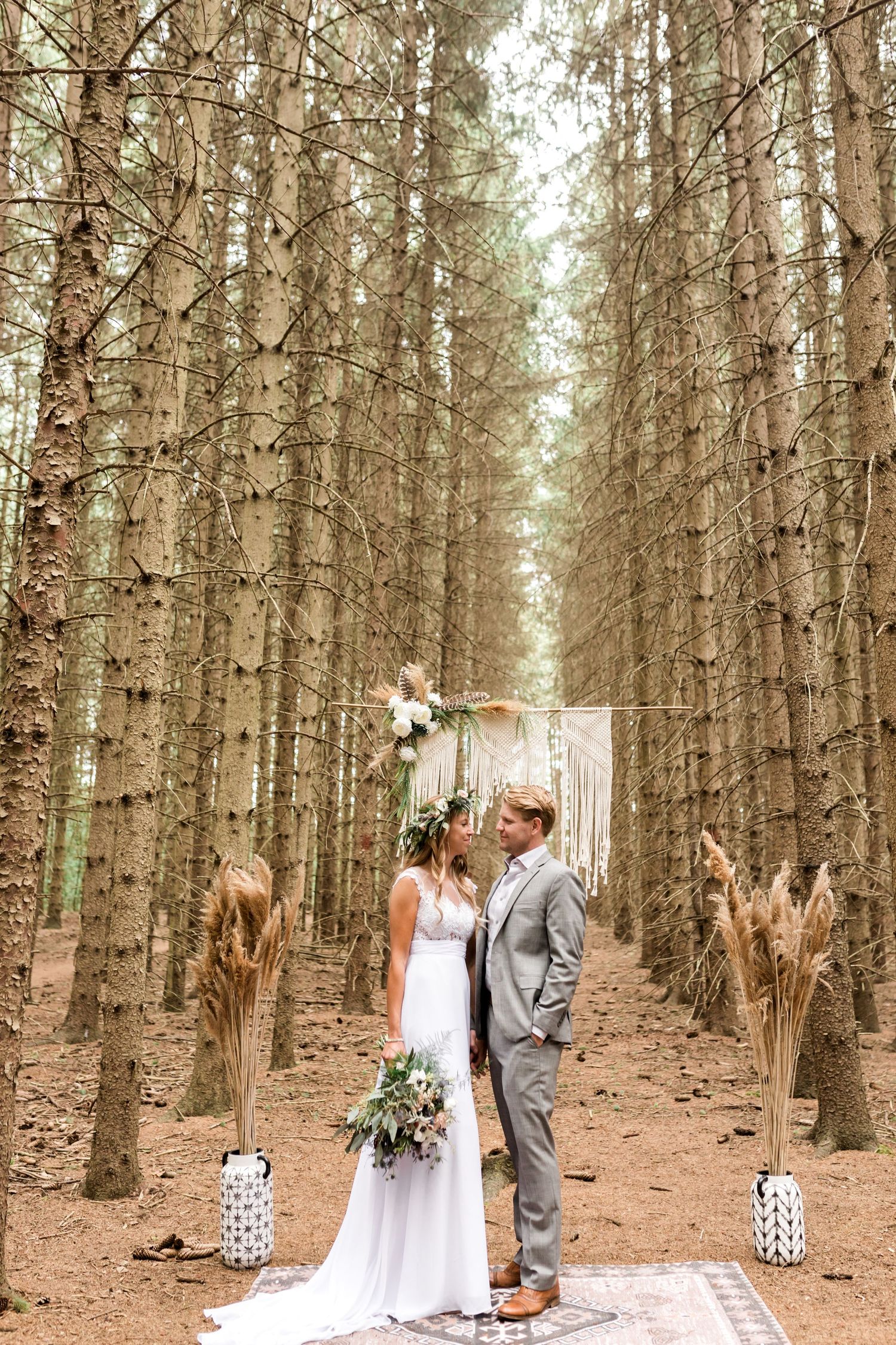 A woodland wedding ceremony setup with lanterns and white fabric between tall pine trees.