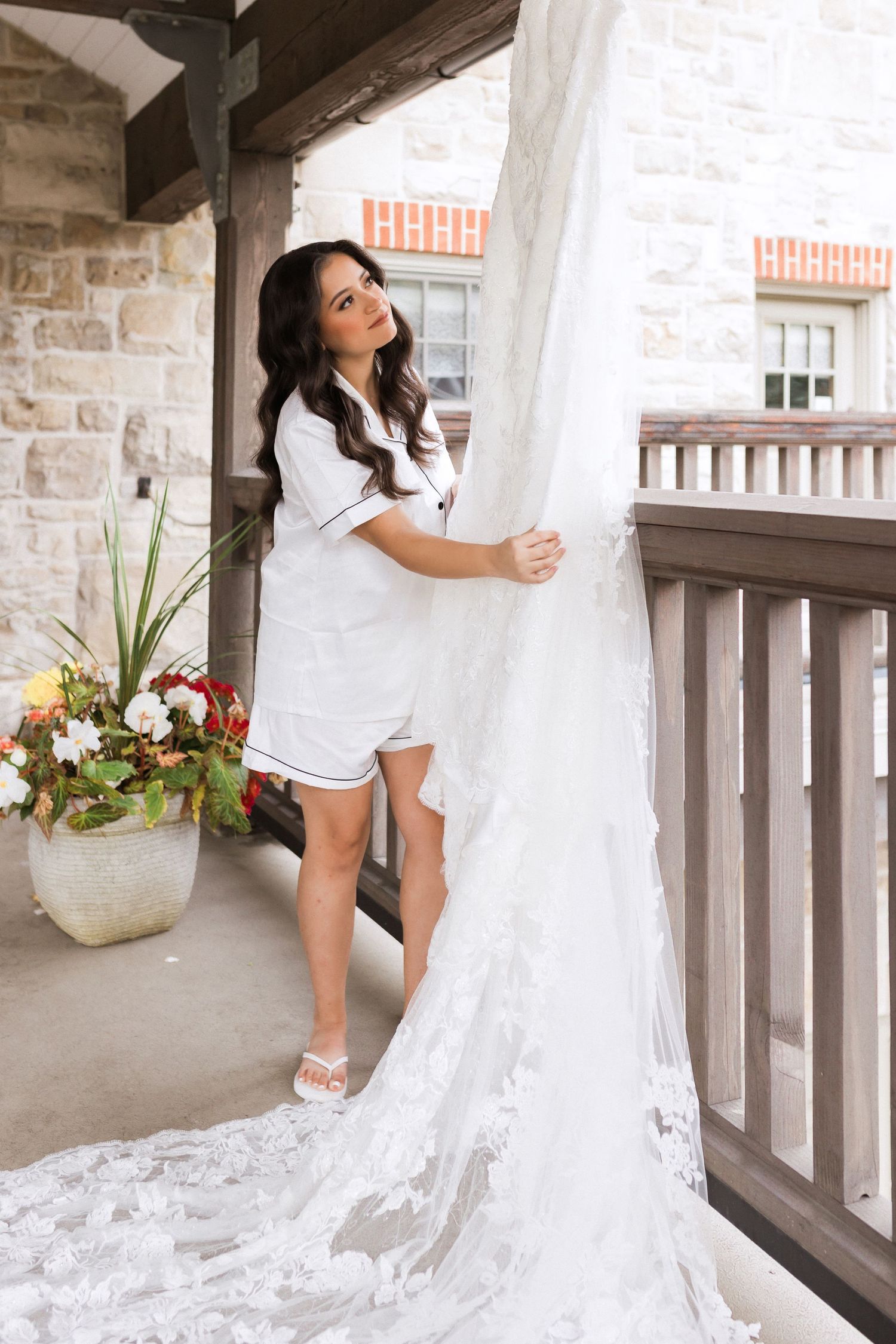 Wedding dress preparation scene on stone porch with floral arrangements.