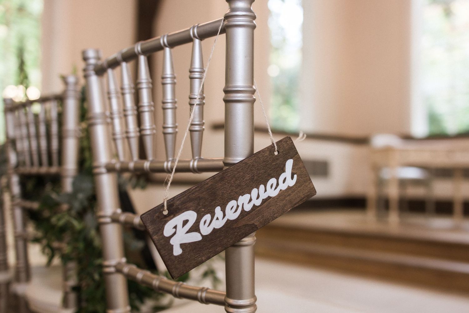 Close-up of a vintage-style 'Reserved' sign hanging on a silver Chiavari chair.