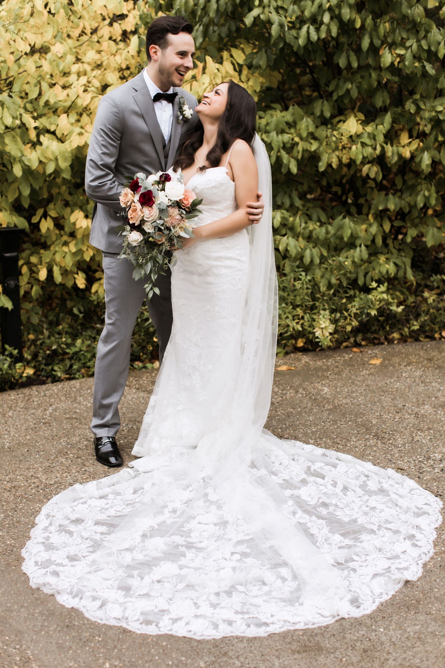 Newlyweds share romantic moment with bride's lace train spread on garden path.