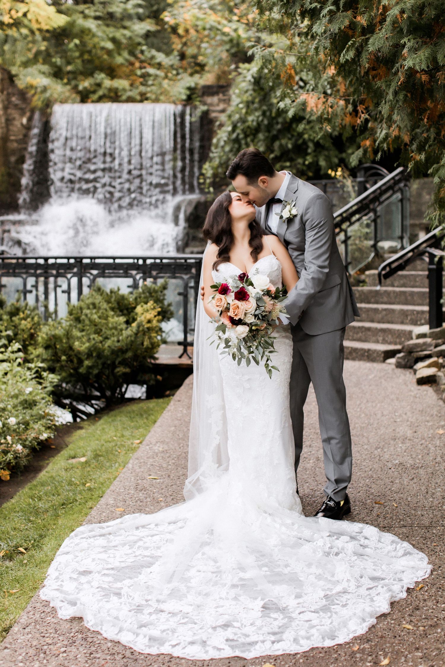 Wedding couple embracing by a waterfall with bride holding floral bouquet.