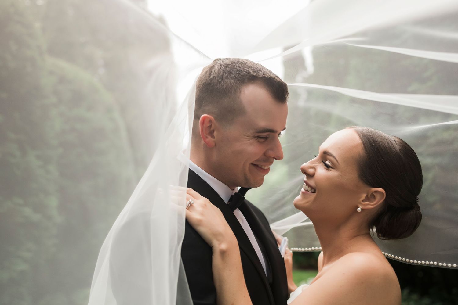 A bride and groom share an intimate moment under a flowing veil during their wedding ceremony.