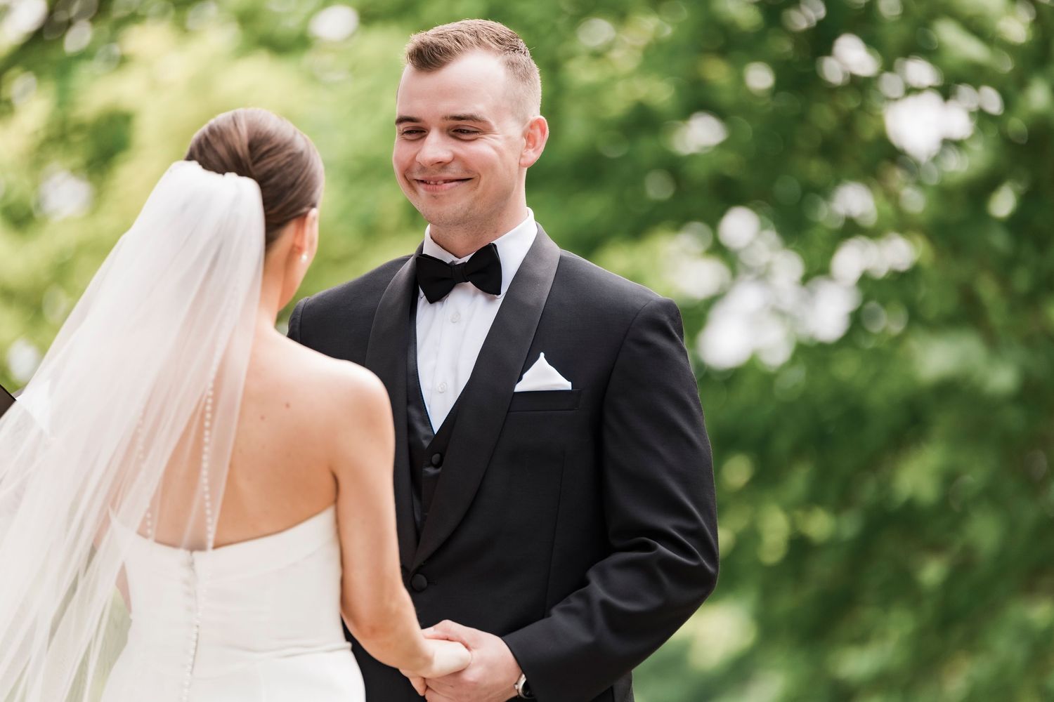 A wedding couple stands together during their outdoor ceremony surrounded by lush green foliage.