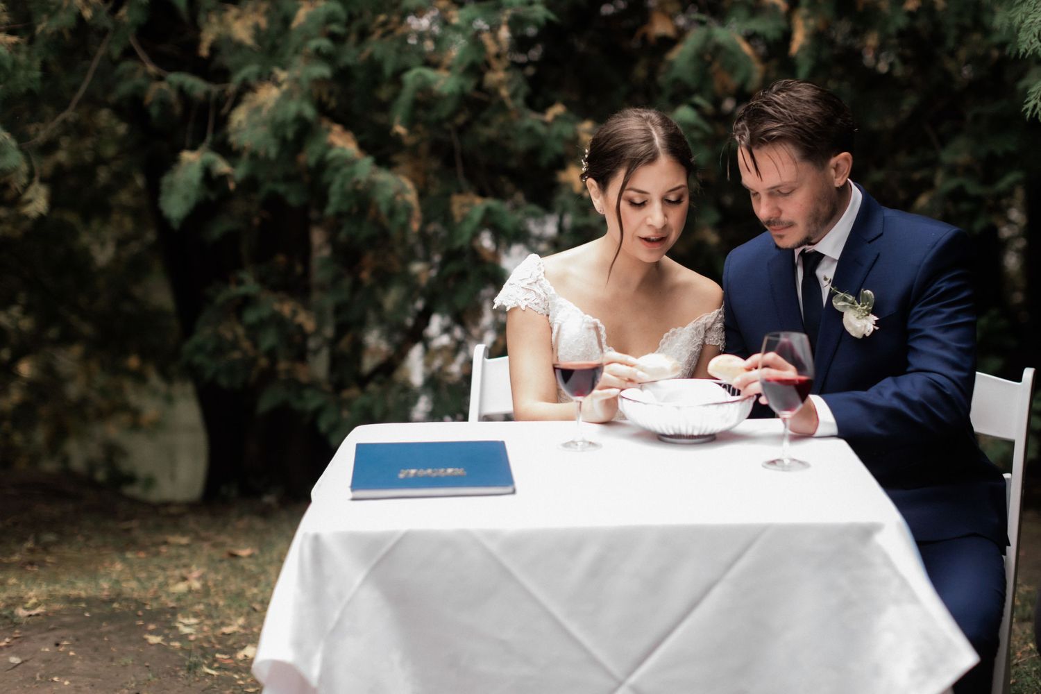 Newlyweds sit at a white-clothed table during their wedding reception signing documents.