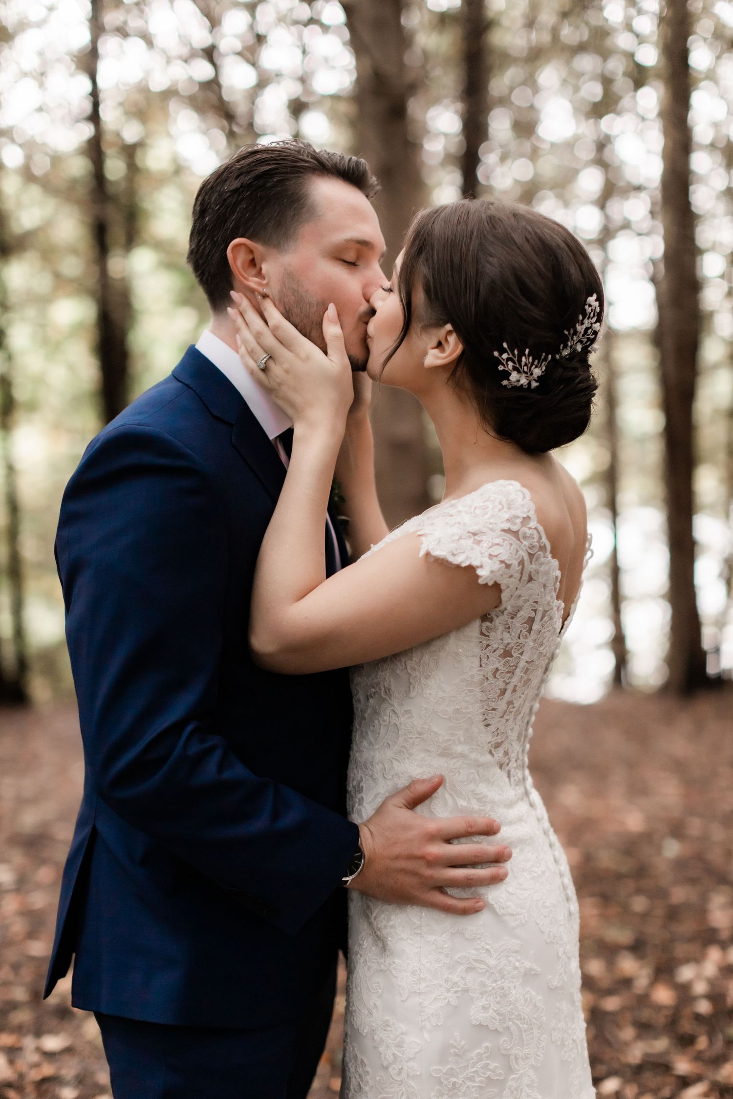 Romantic wedding couple sharing a tender kiss in a forest setting with beautiful natural lighting and fall foliage.