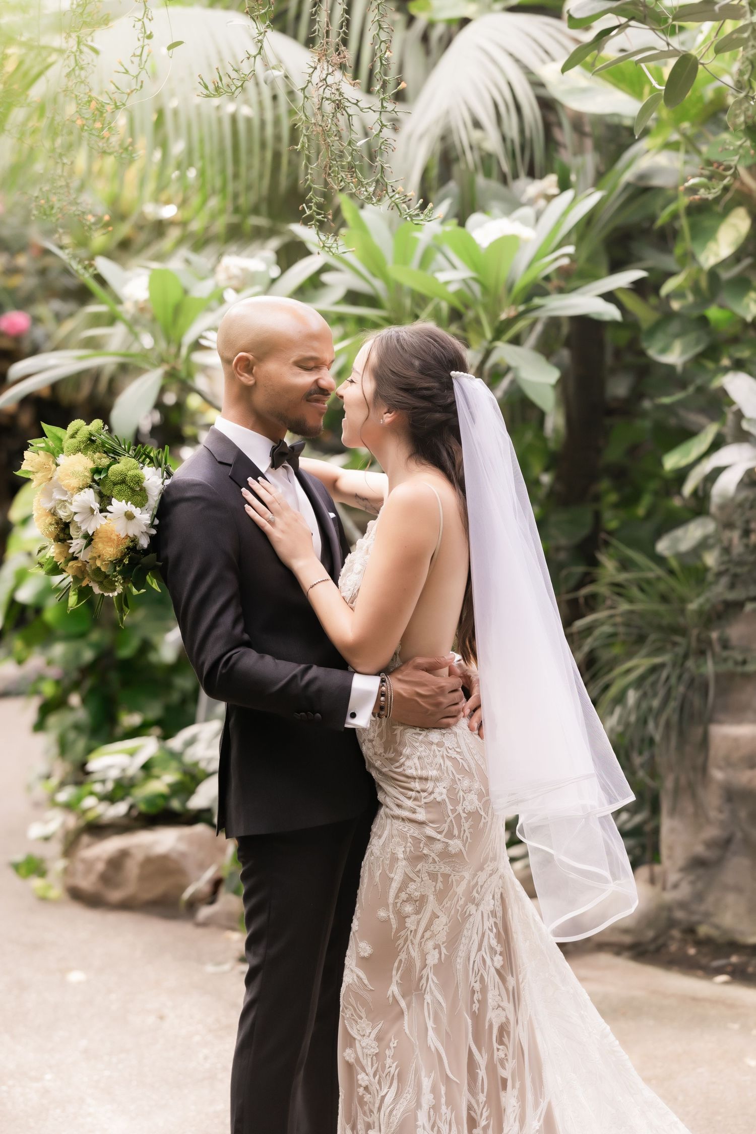 Romantic wedding moment captured as couple shares a tender embrace surrounded by lush tropical plants.