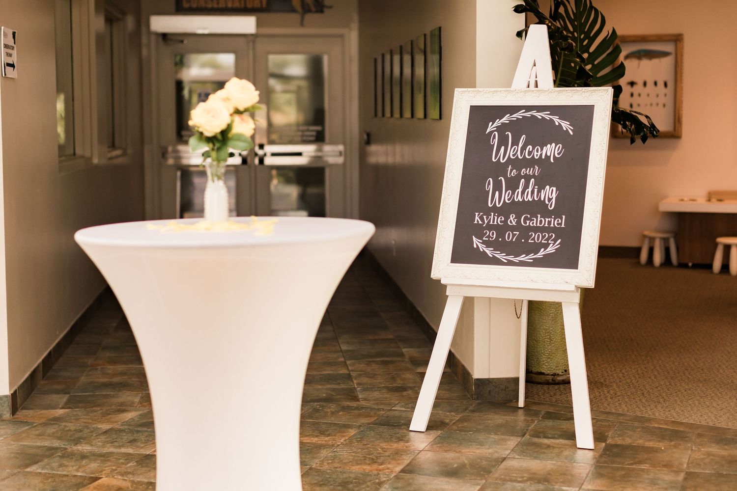 Wedding welcome sign on easel next to white cocktail table with floral centerpiece.