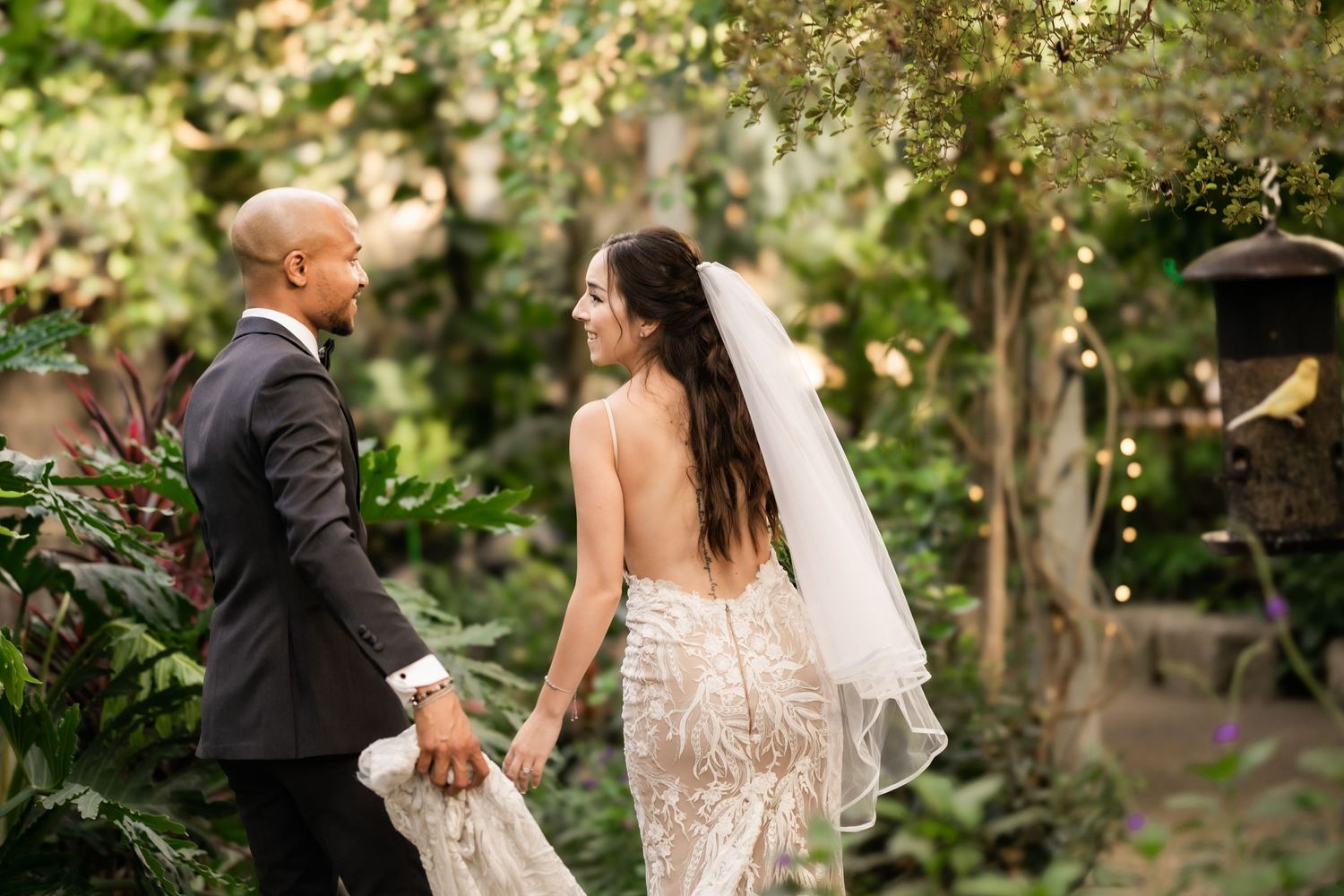 Bride and groom holding hands in front of green foliage in elegant garden setting.