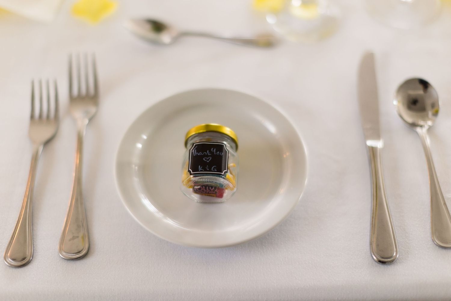 Close up of formal place setting with small jar favor on white plate.