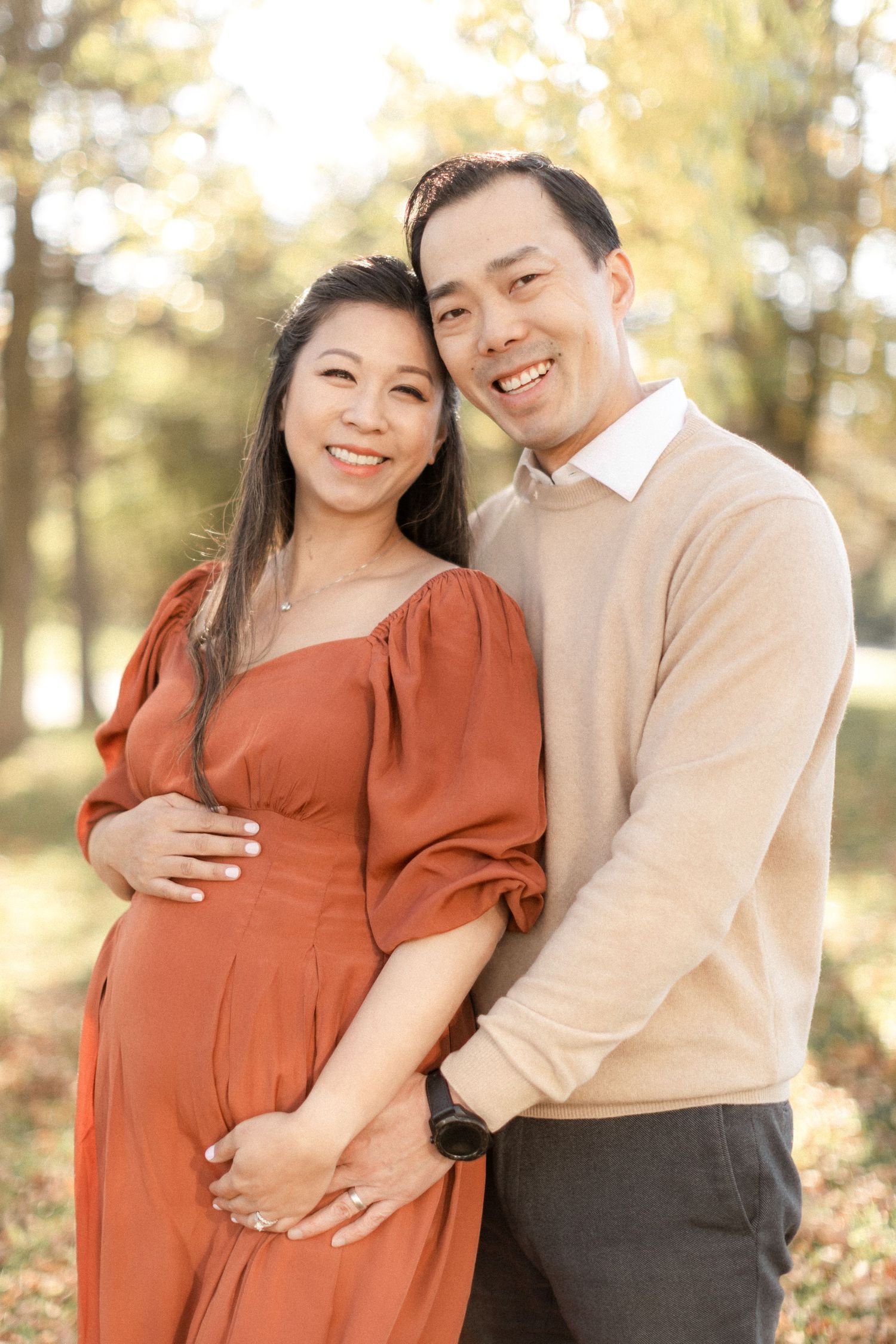 Happy couple poses for maternity photos in warm autumn setting.