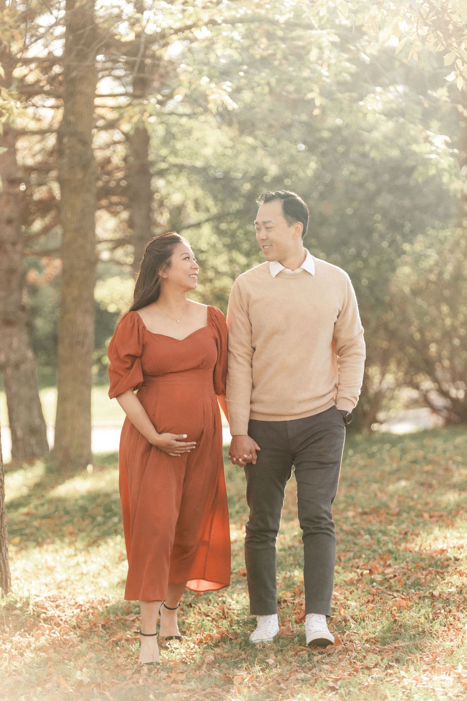 A couple takes a romantic stroll through an autumn park during their maternity photoshoot.