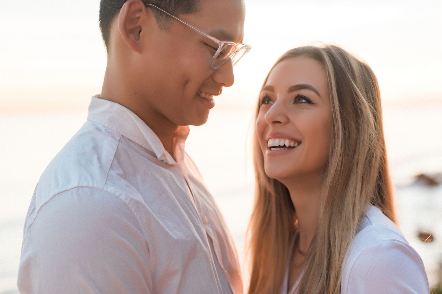 Close-up of couple smiling at each other against ocean backdrop.