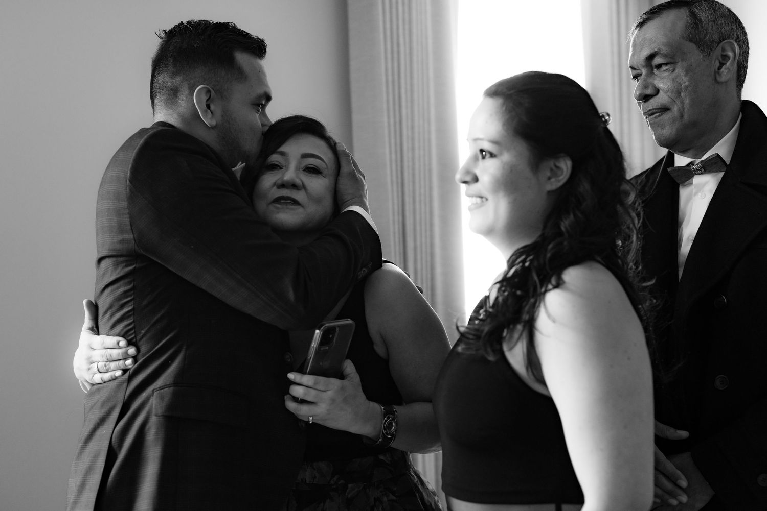 Emotional wedding guests share hugs and tears during reception in formal attire.