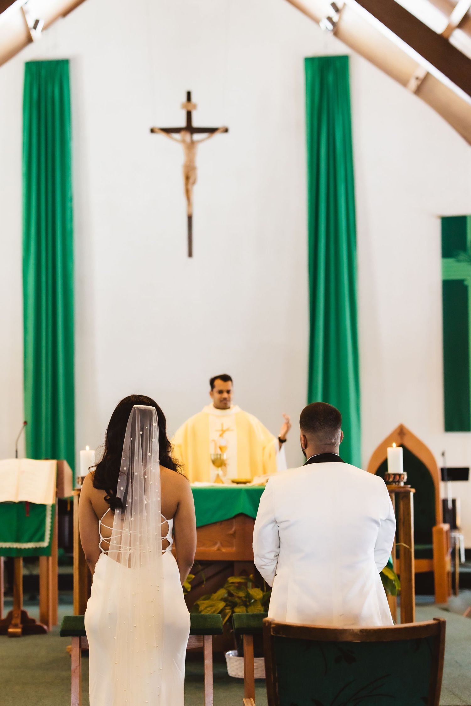 A wedding ceremony in progress at a church with green curtains and wooden pews.