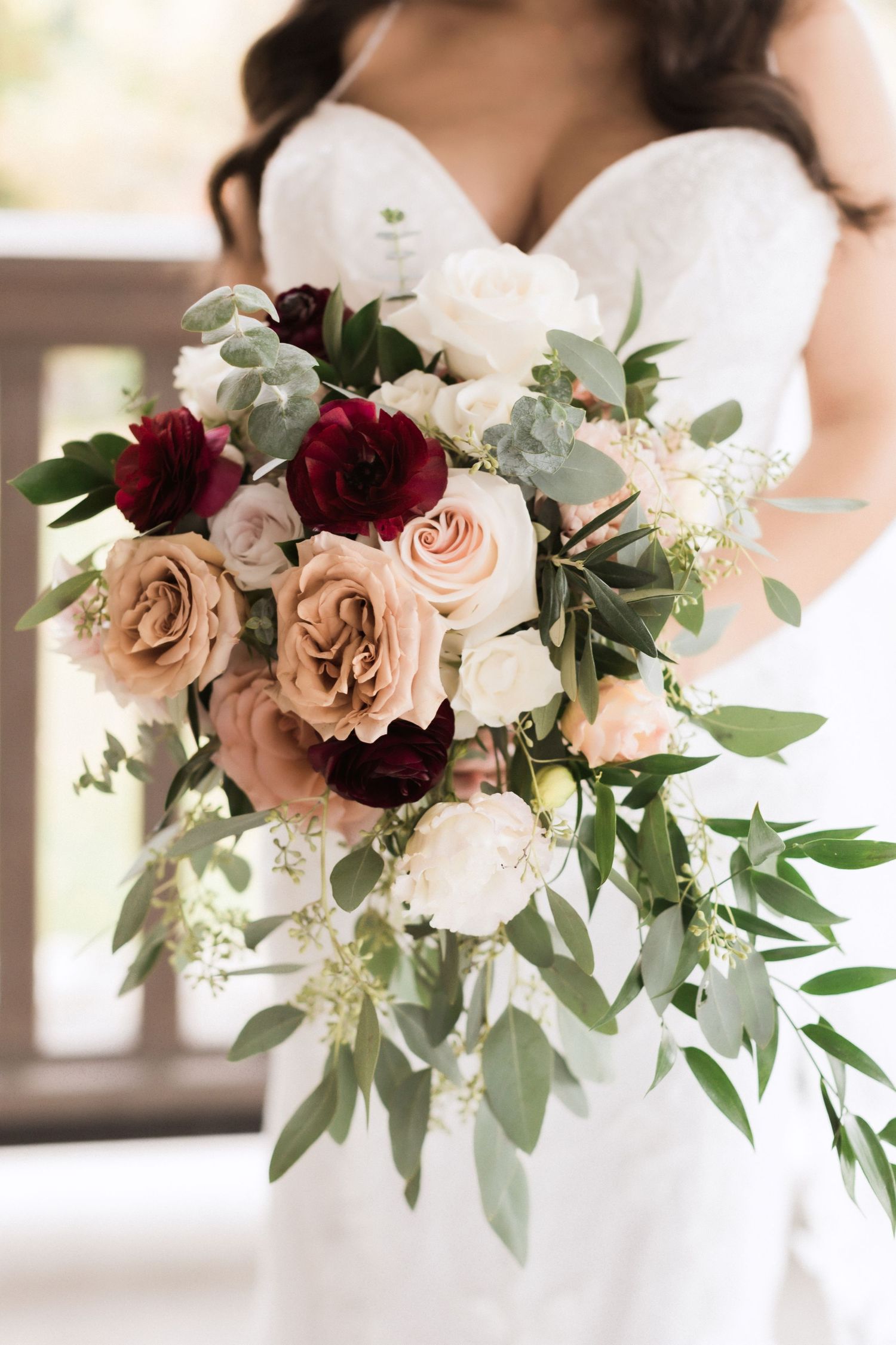 Elegant bridal bouquet with burgundy and blush roses against white wedding dress.