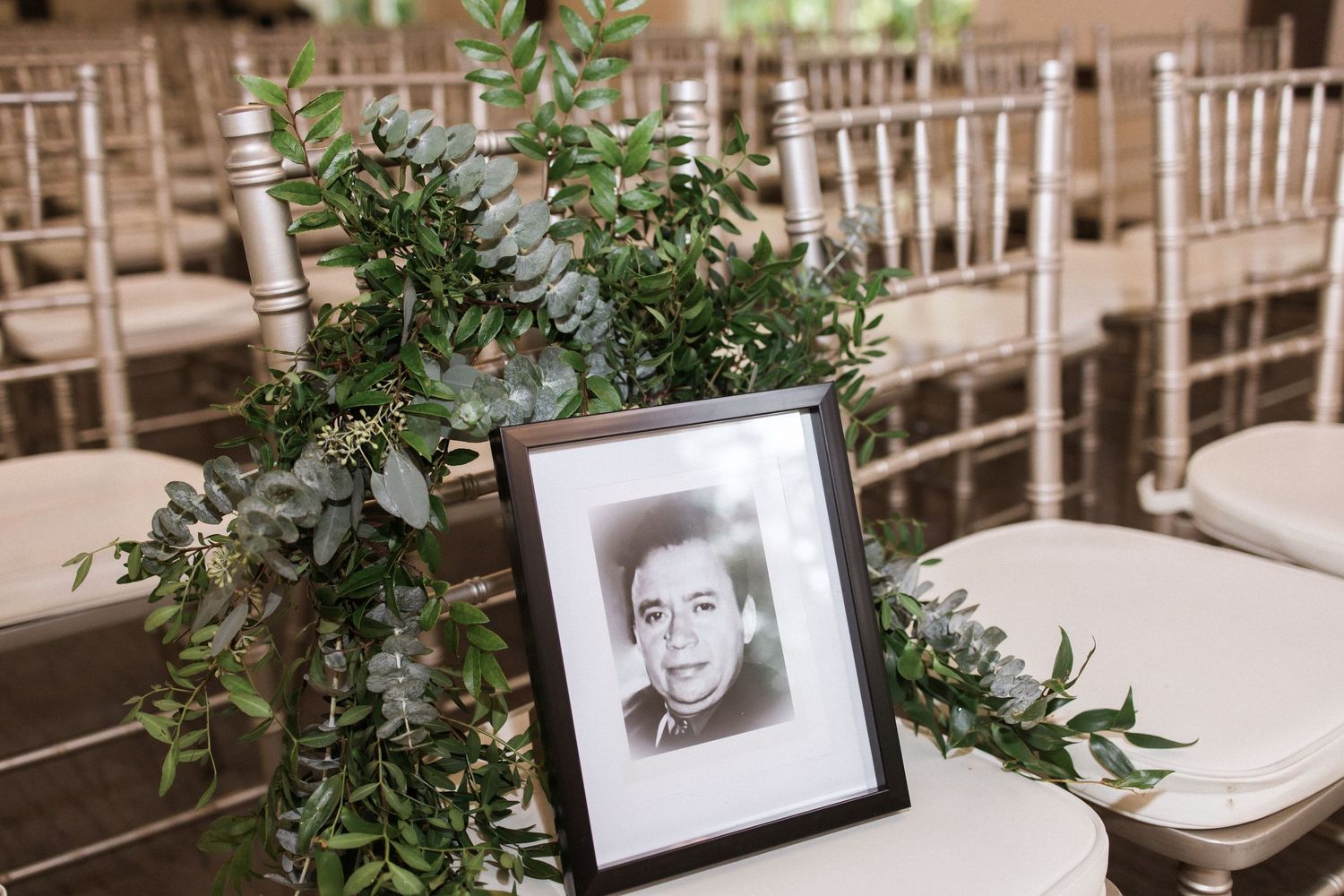 Wedding ceremony decor featuring framed portrait with greenery arrangement on Chiavari chair.