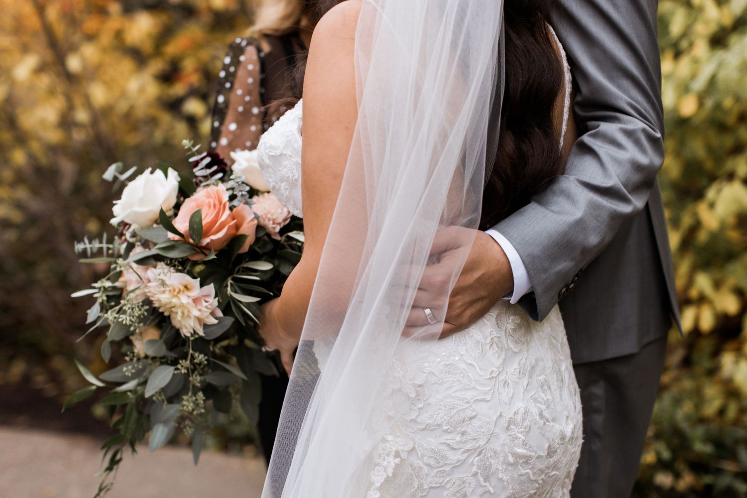 Close-up of wedding couple with lace dress details and elegant floral bouquet.