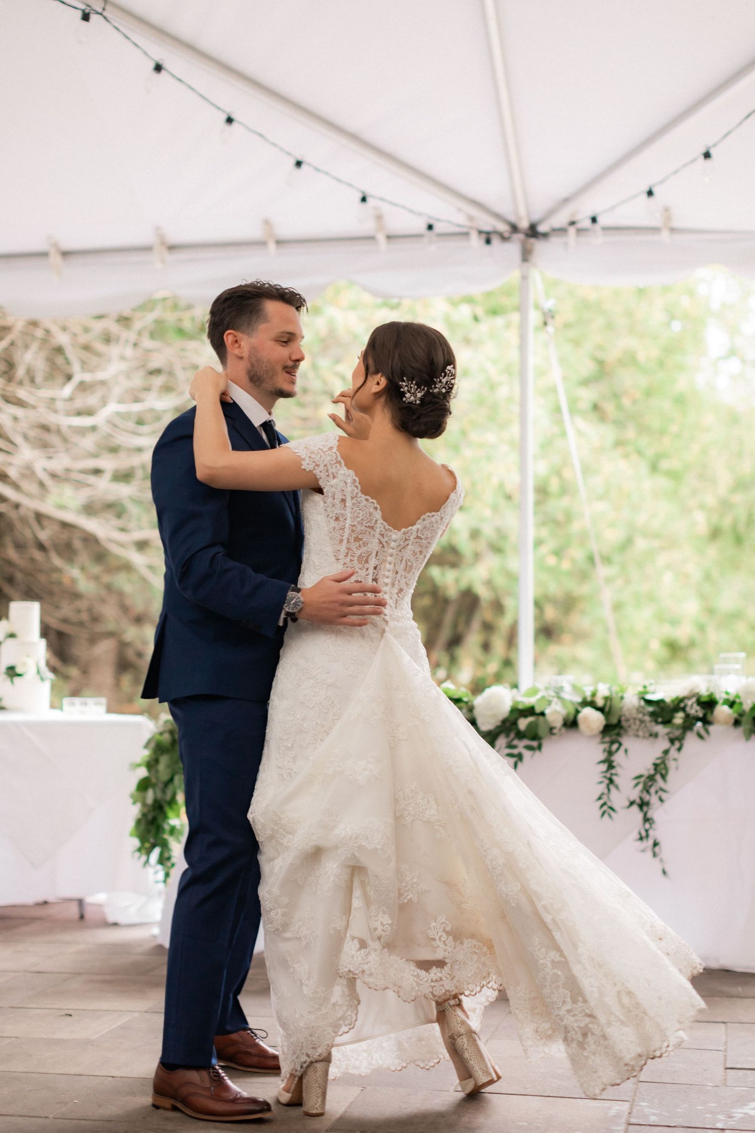 Couple dancing under white tent with flowing lace wedding dress and navy suit.
