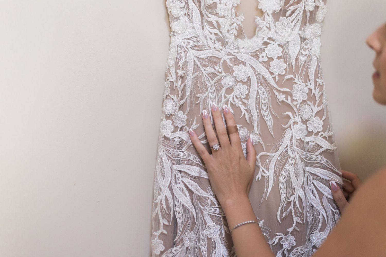 Close-up of hand touching intricate lace details on white wedding dress.