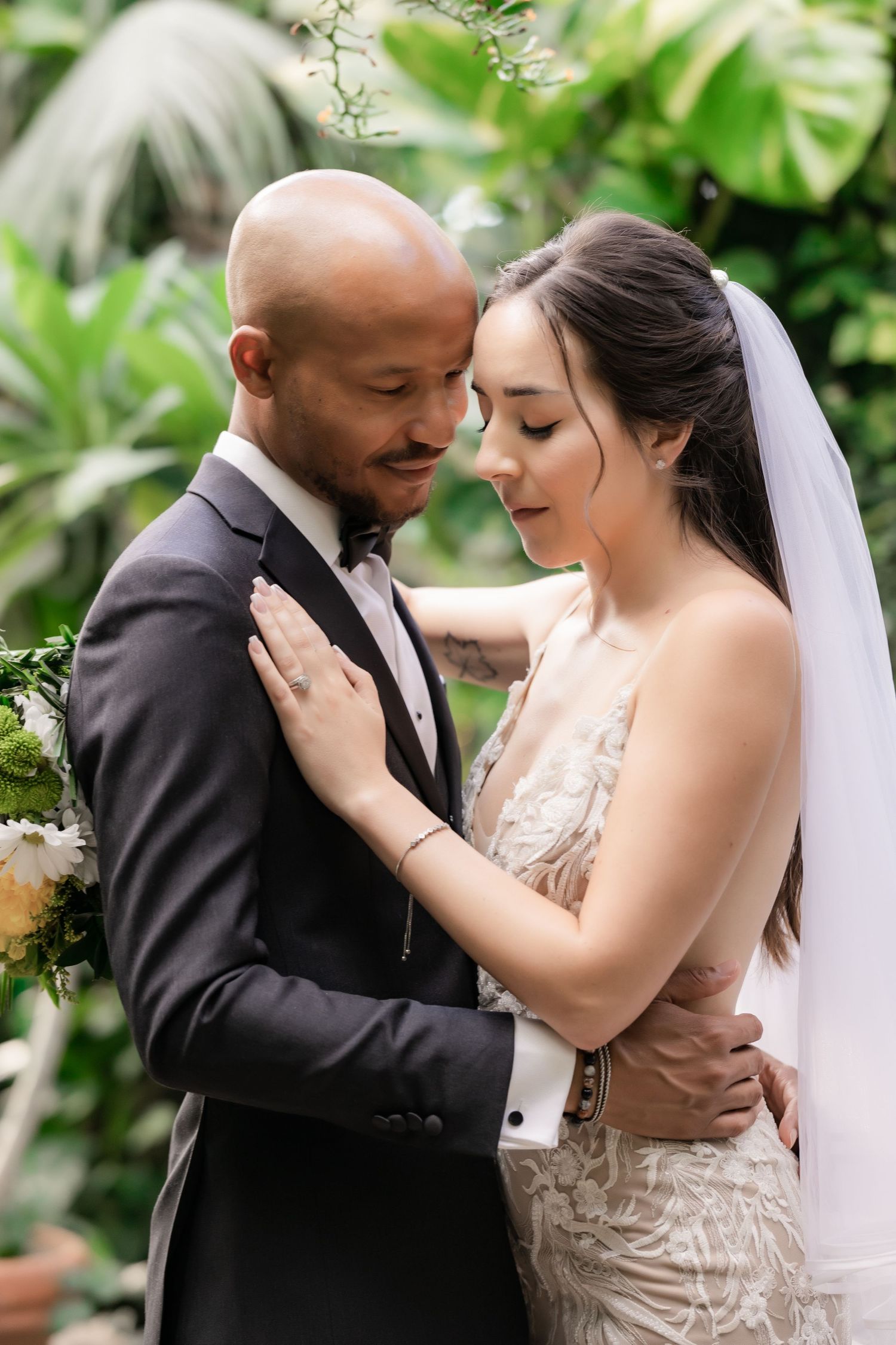 Tender wedding portrait with couple embracing against a backdrop of tropical greenery.