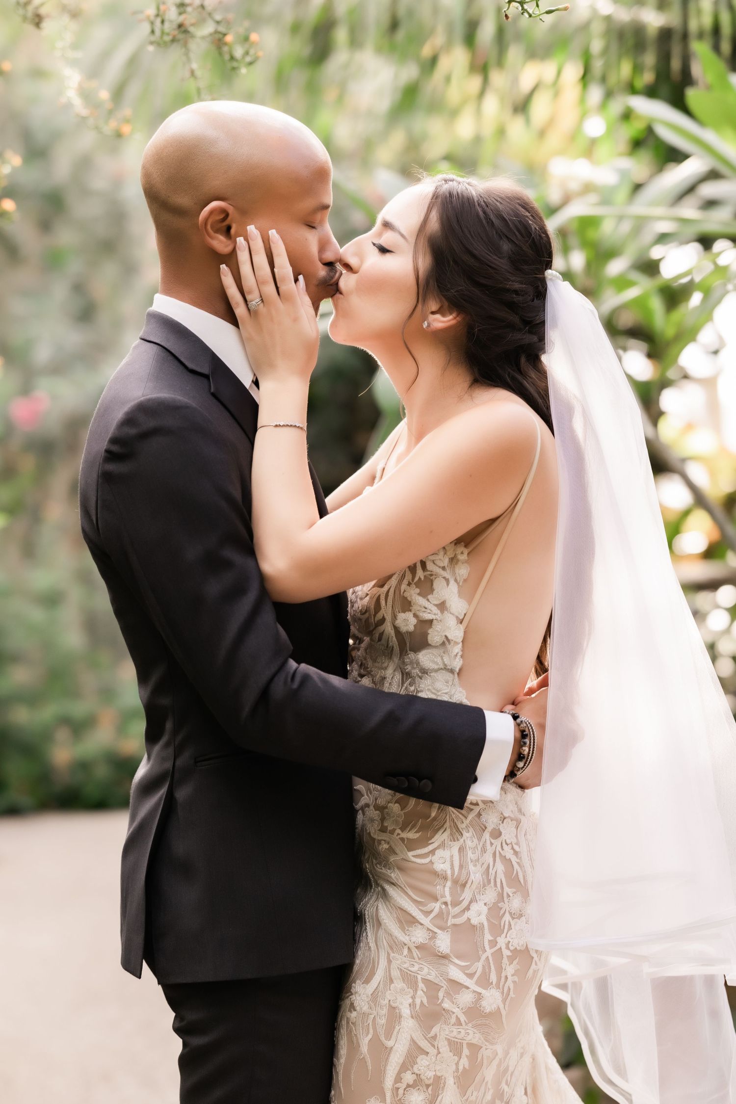 Romantic wedding kiss captured in a lush greenhouse with soft natural lighting.