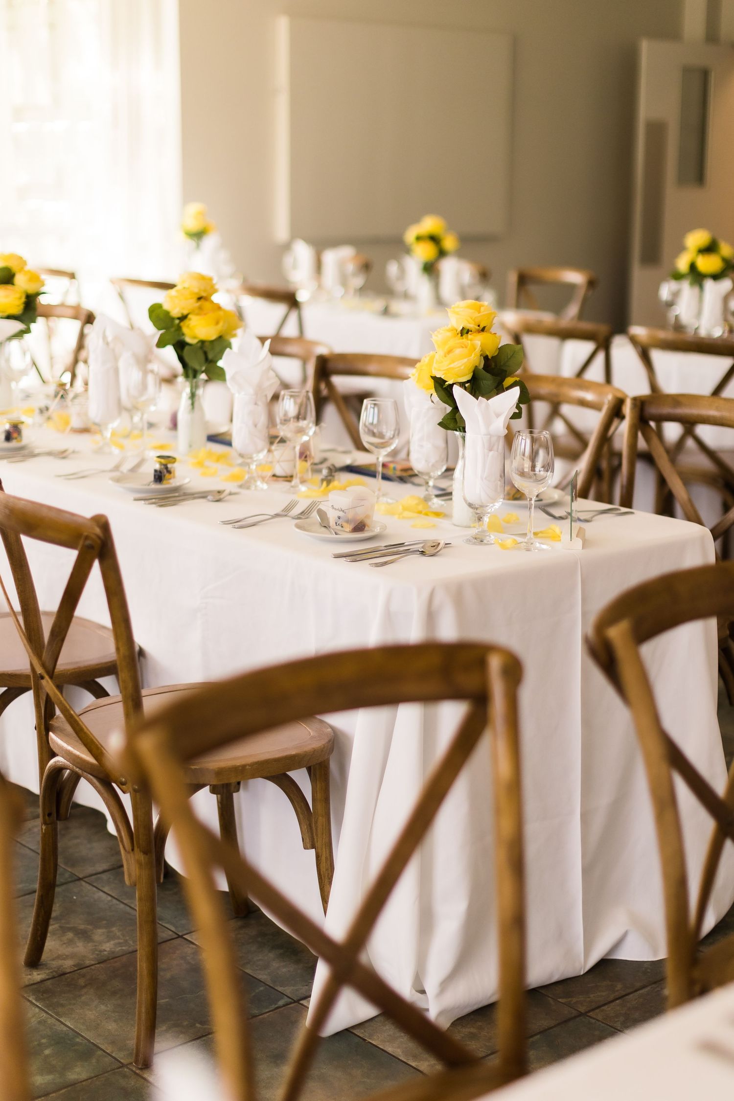 Wedding reception dining area with white tablecloths and yellow rose centerpieces.