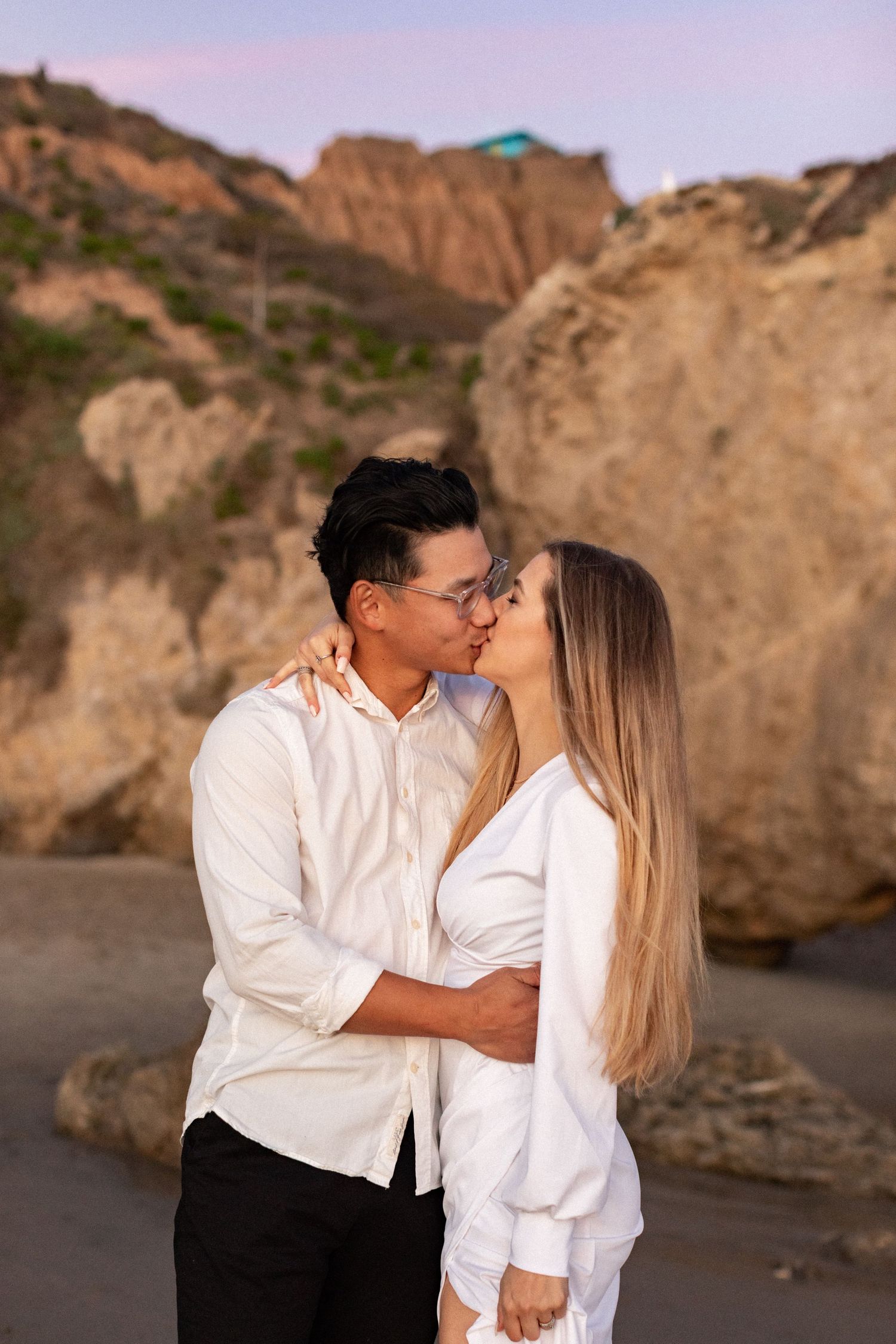 Romantic couple sharing tender moment against coastal cliff backdrop.