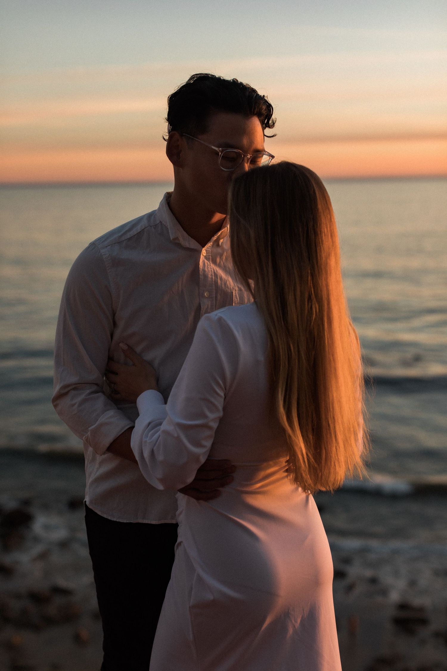 Silhouetted couple in white embraces against dramatic ocean sunset.