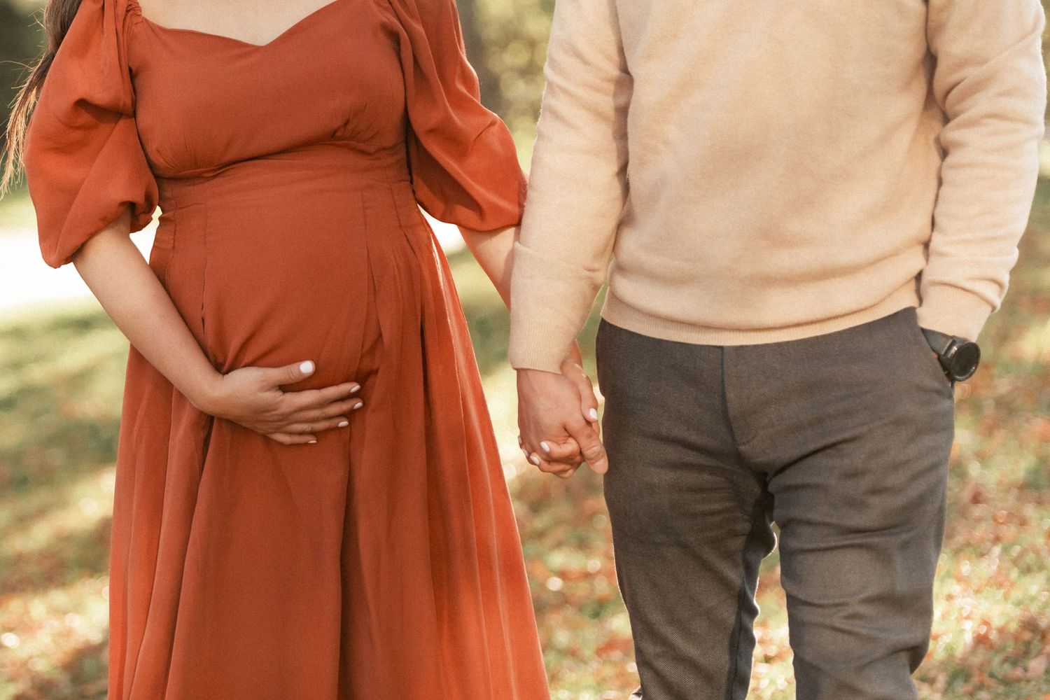 A close-up shot highlighting a pregnancy bump with couple holding hands in complementary outfits.