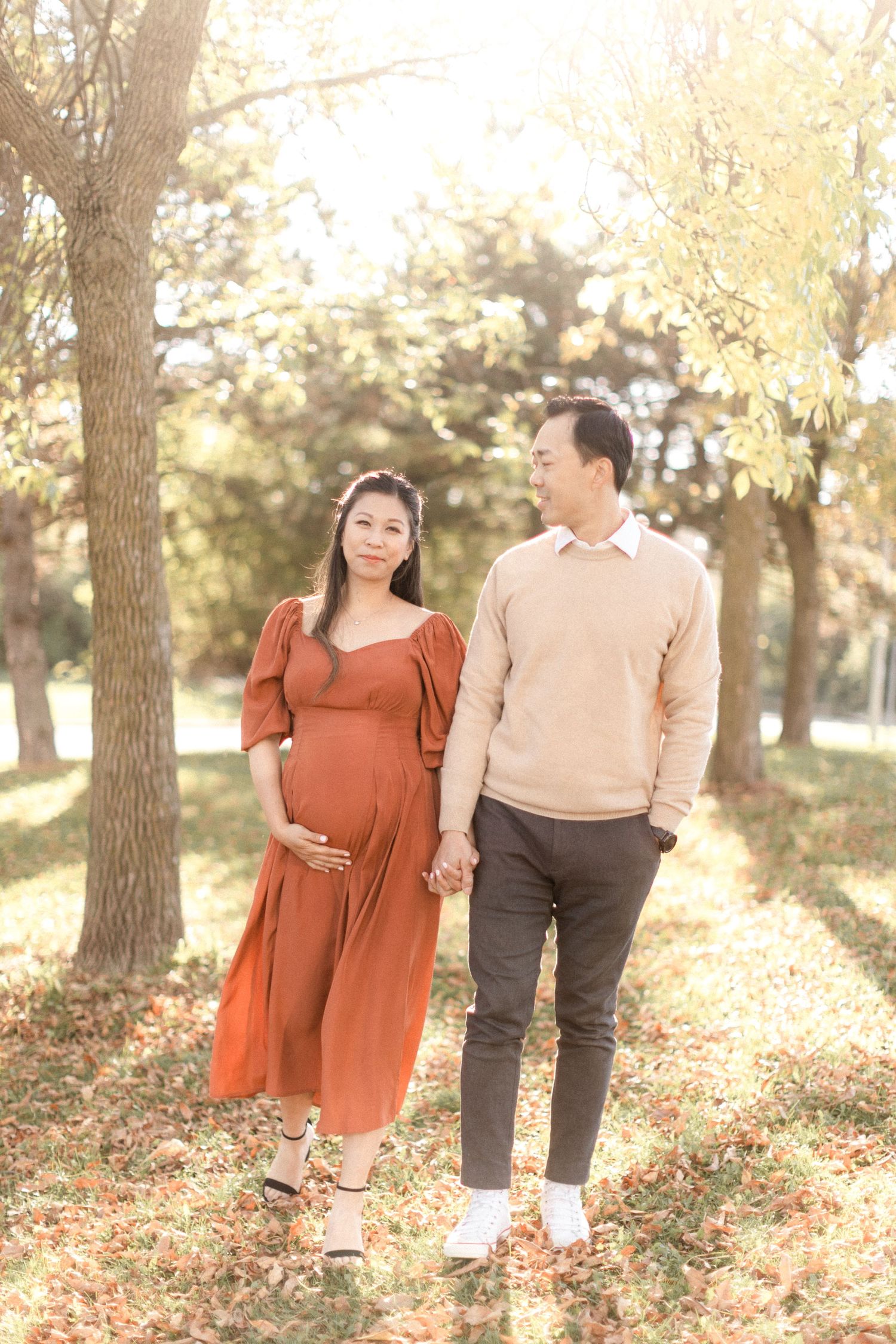 Romantic maternity portrait of couple standing in golden autumn forest light.