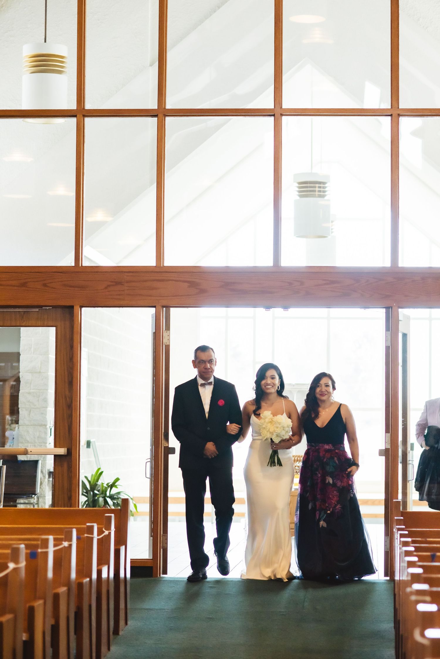 A procession walks down the church aisle with tall windows and wooden architectural details.