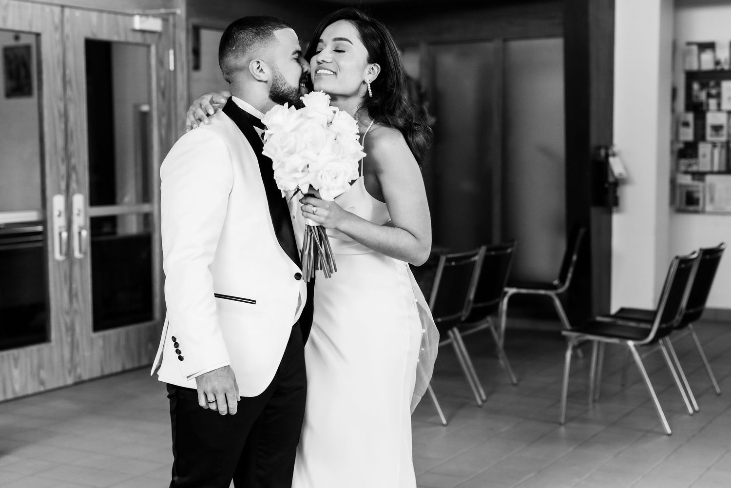 Black and white photo of bride and groom sharing romantic moment with bouquet.