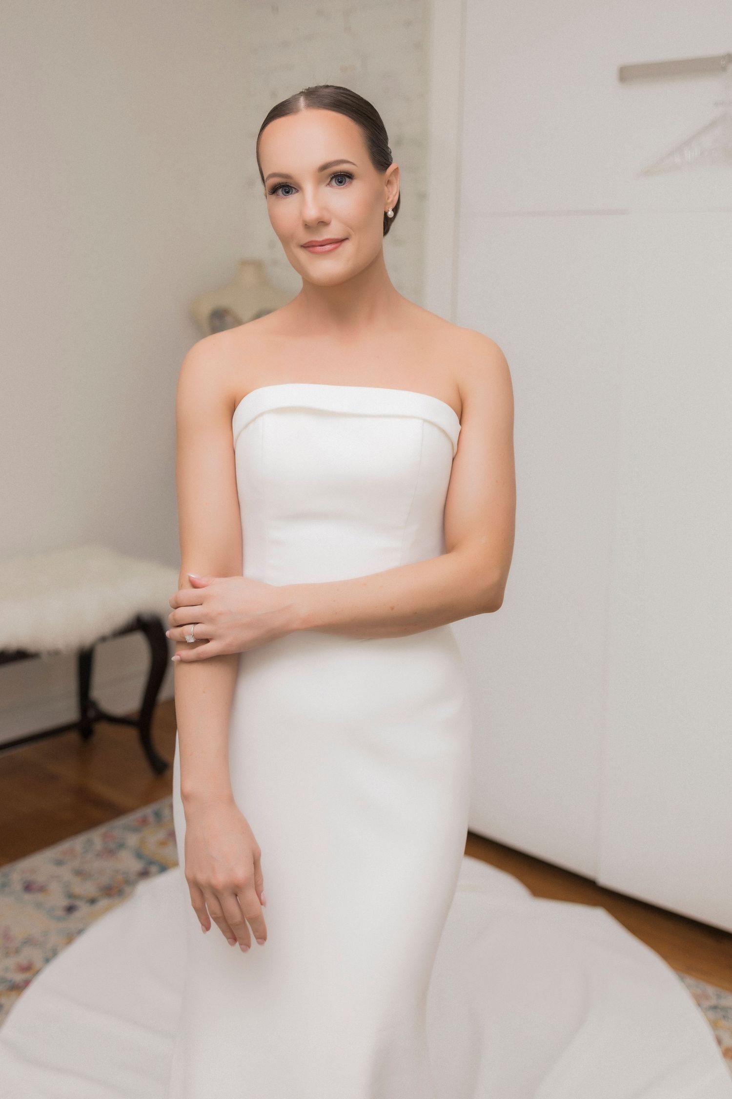 An elegant white strapless wedding dress with a sleek silhouette and minimalist design in a light-filled room.