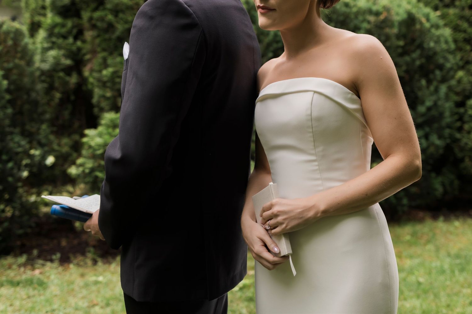 A close up shot of newlyweds standing together in a garden, the bride wearing an elegant strapless white gown.