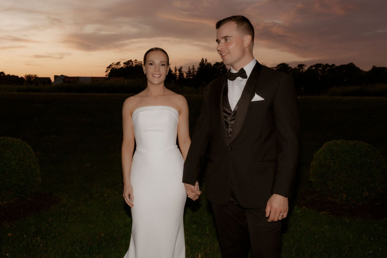 A romantic couple poses together against a dramatic sunset sky during their elegant outdoor wedding photo session.
