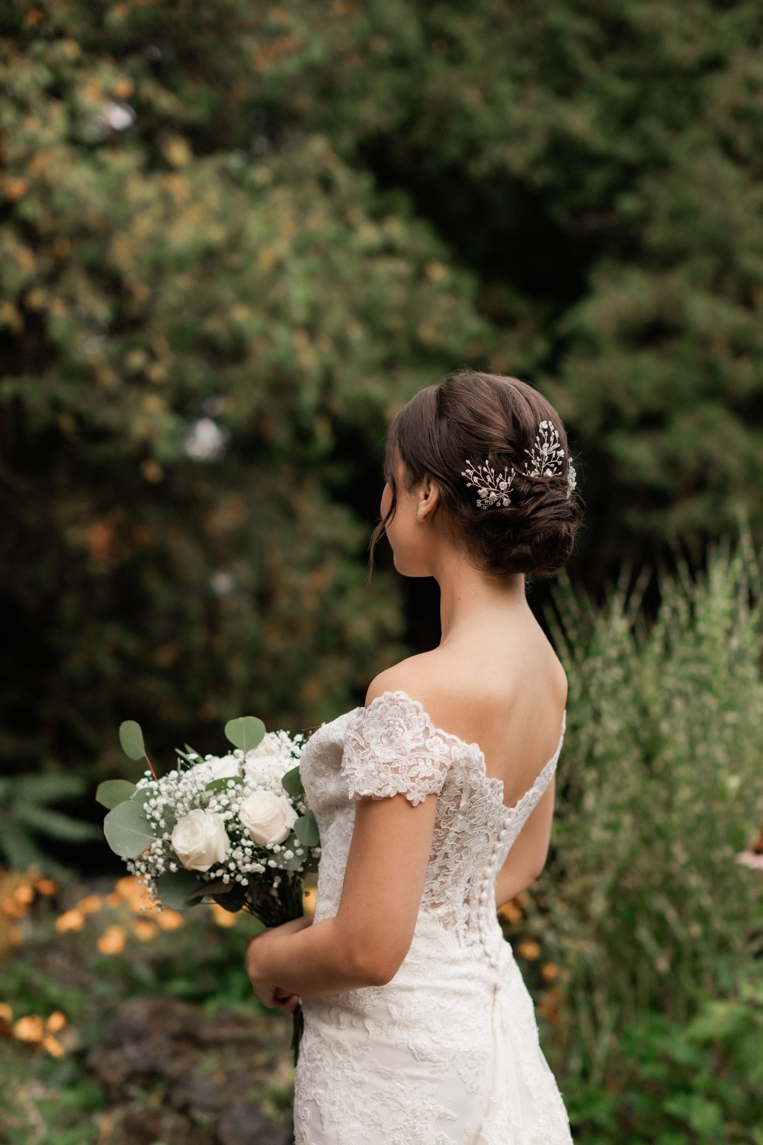 Back view of bride in lace dress holding white bouquet with delicate hair accessory.