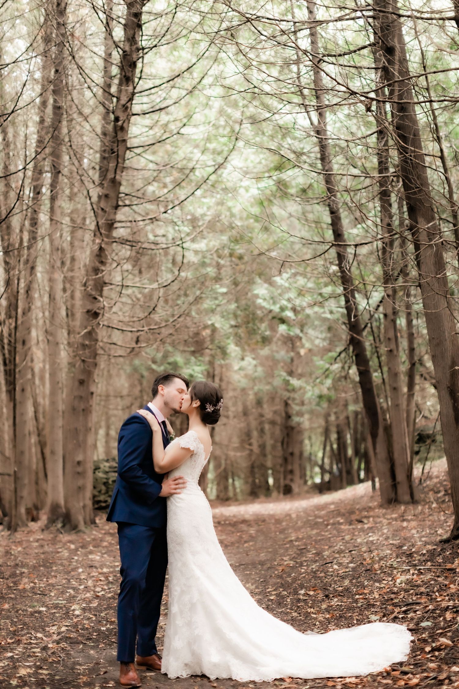 Intimate forest wedding portrait with couple kissing among tall trees.
