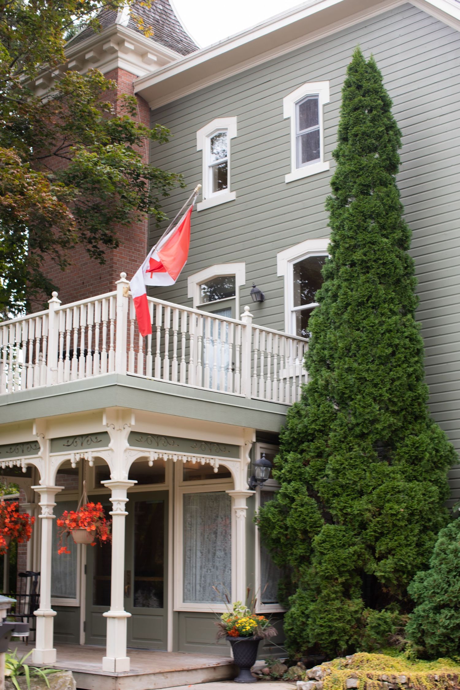 Victorian style house with Canadian flag and white porch decorated with hanging flowers.
