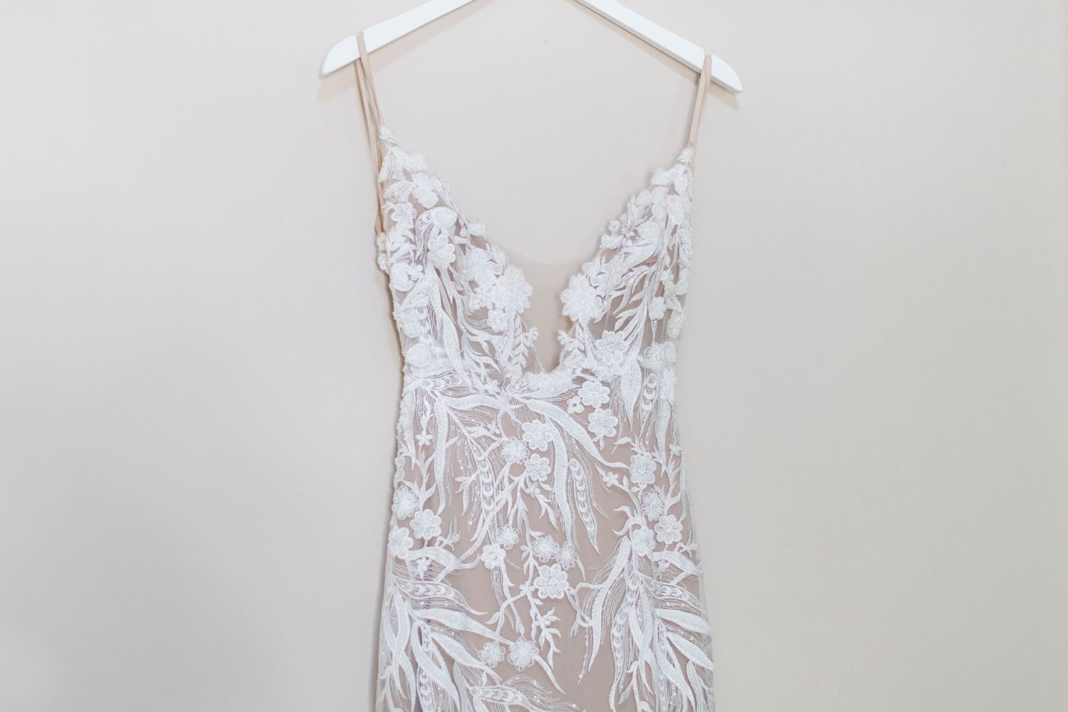 White lace wedding dress with intricate floral pattern hanging on display.