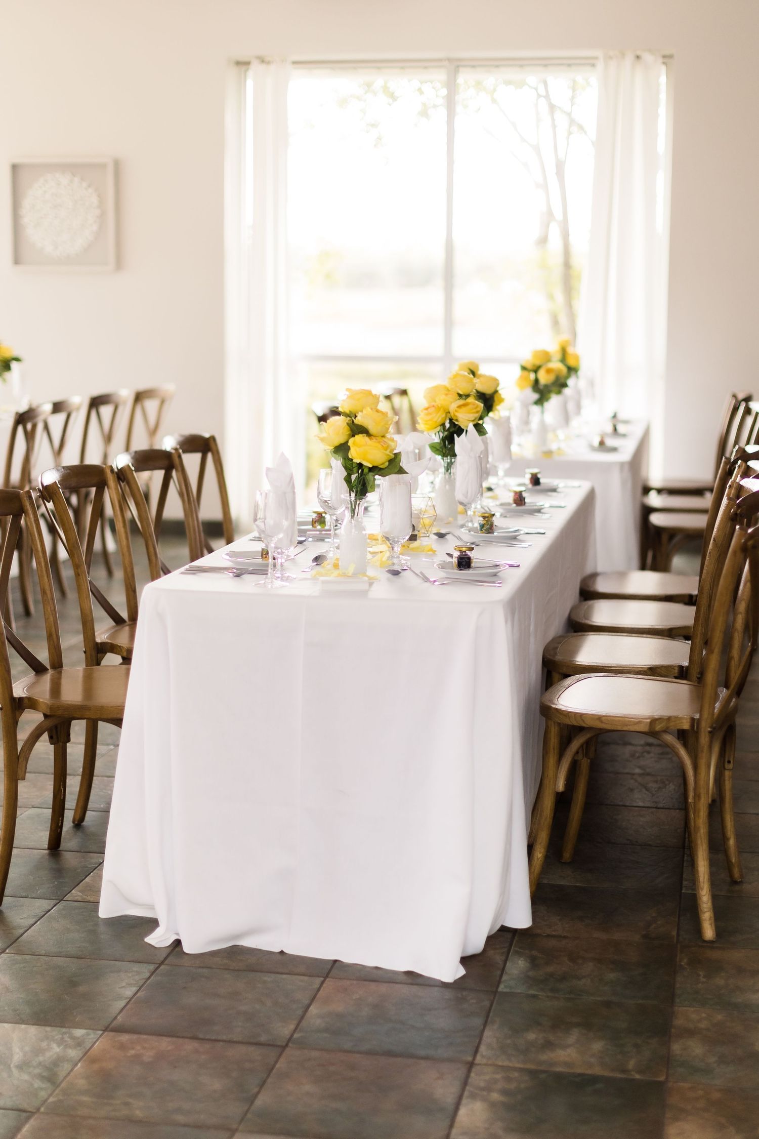 Elegant wedding reception table with bright yellow floral arrangements and natural light from windows.